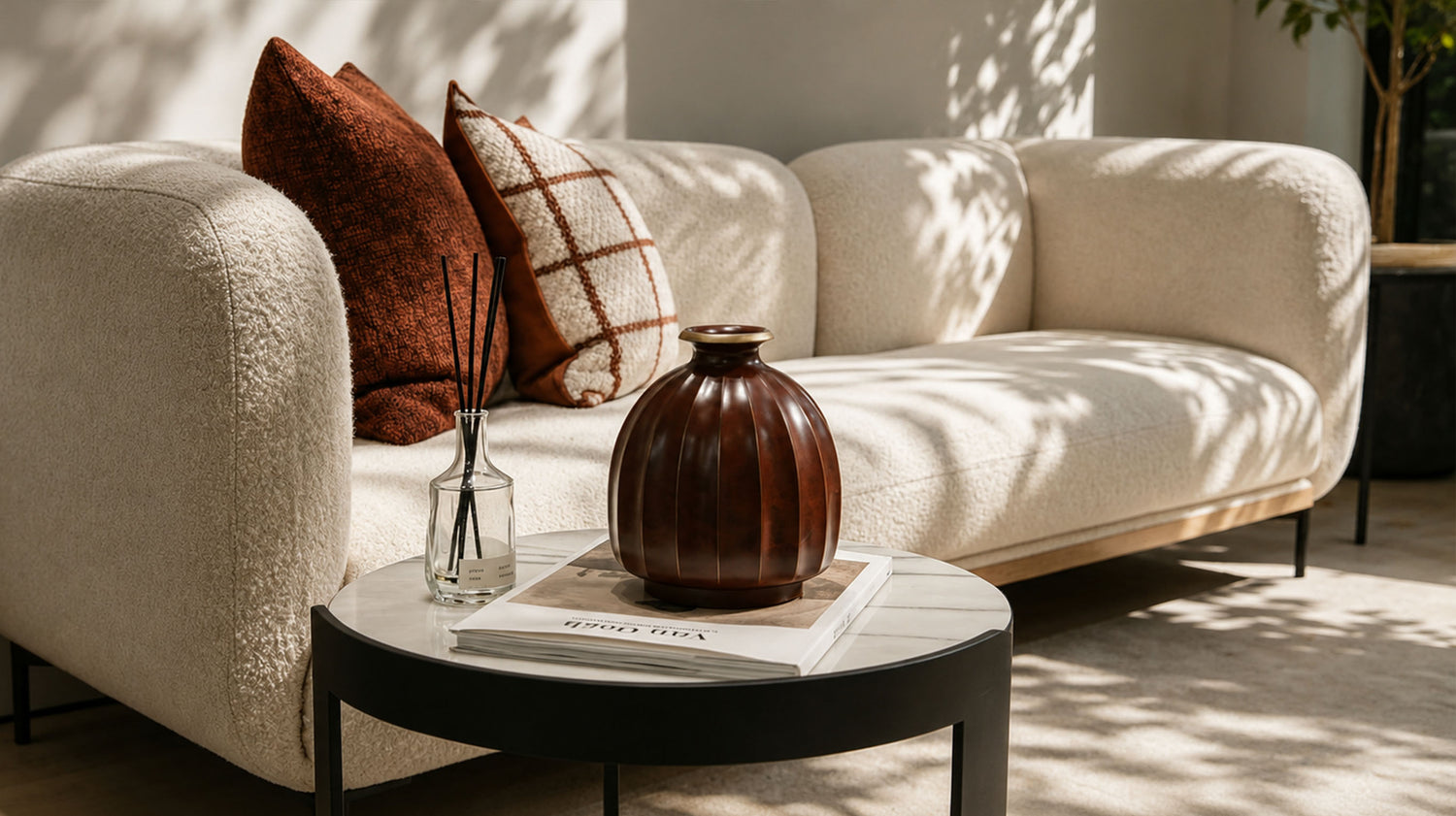 Artamore artistic living scene with a brown sculptural vase, reed diffuser, coffee table and warm sofa in natural sunlight.