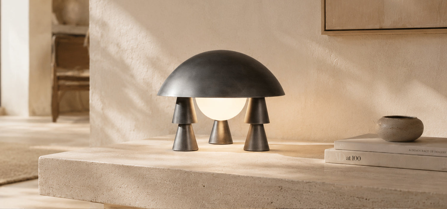 Artamore sculptural table lamp with a black dome shade and glowing orb light styled on a warm stone surface with books and ceramic decor.