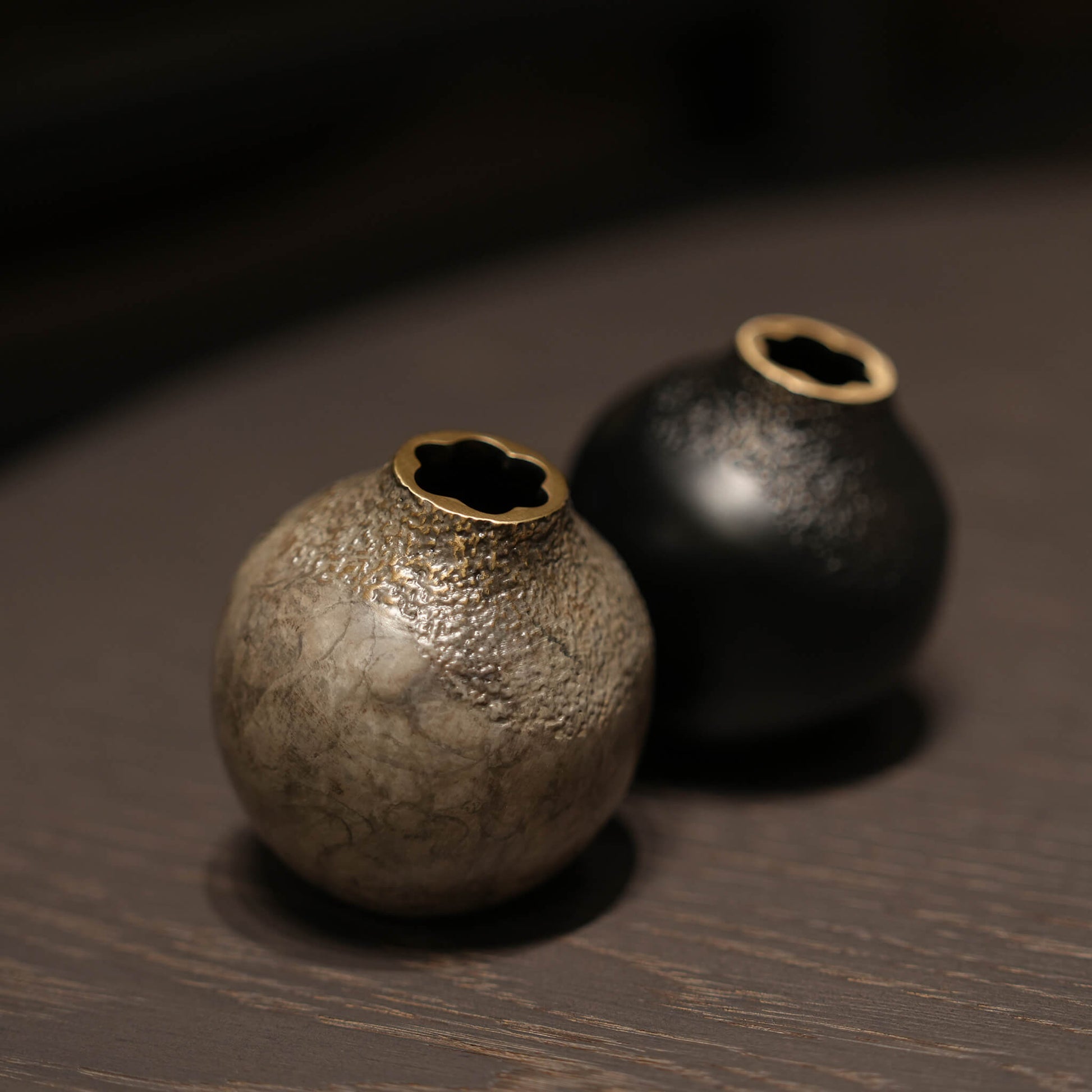 A pair of handcrafted solid brass acorn vases in black and grey, elegantly styled on dark wood furniture