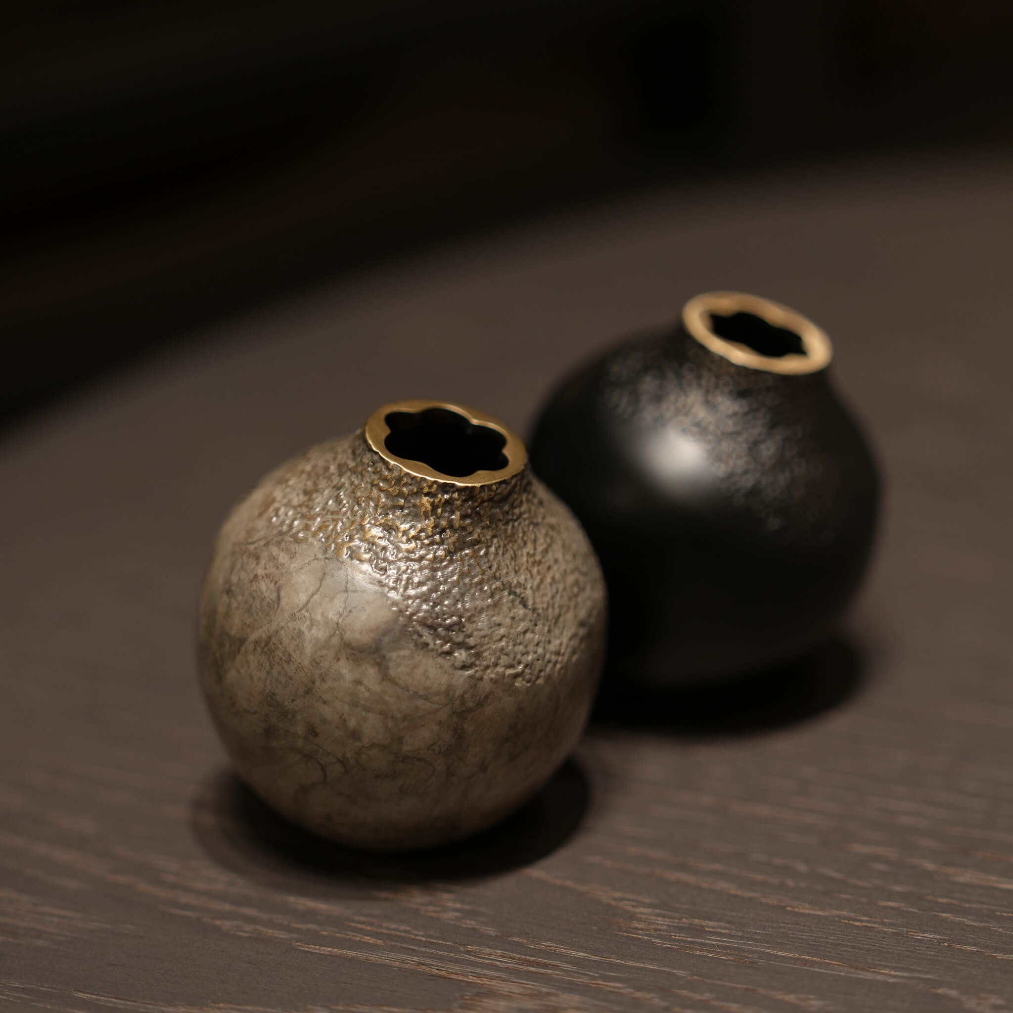 A pair of handcrafted solid brass acorn vases in black and grey, elegantly styled on dark wood furniture