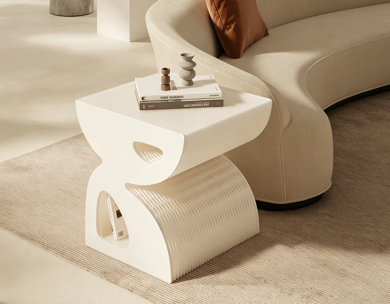 Artamore sculptural white side table styled with books and decorative objects beside a curved cream sofa.