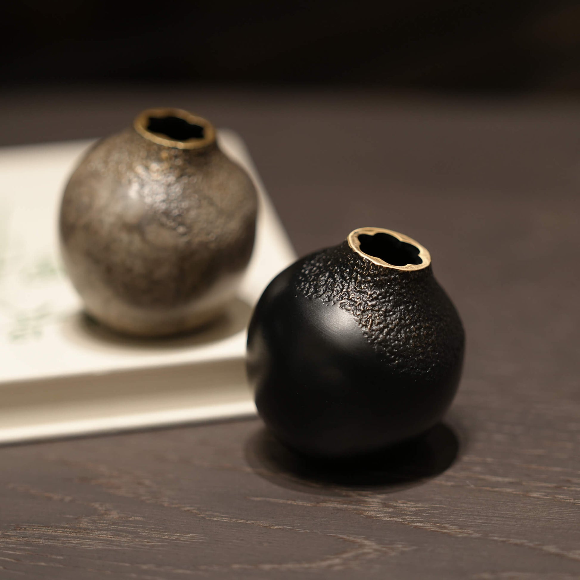A pair of solid brass acorn vases in black and grey styled on a book, demonstrating minimalist European aesthetic decor