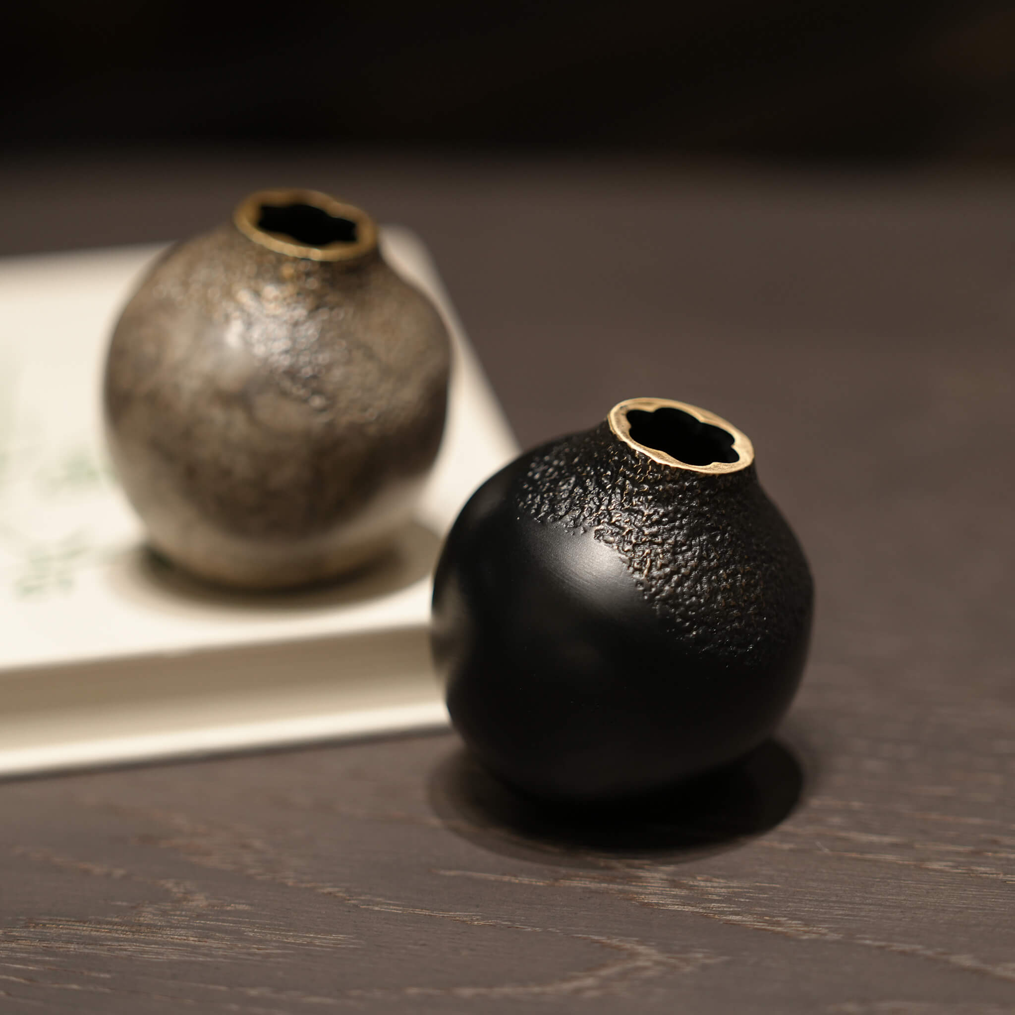 A pair of solid brass acorn vases in black and grey styled on a book, demonstrating minimalist European aesthetic decor