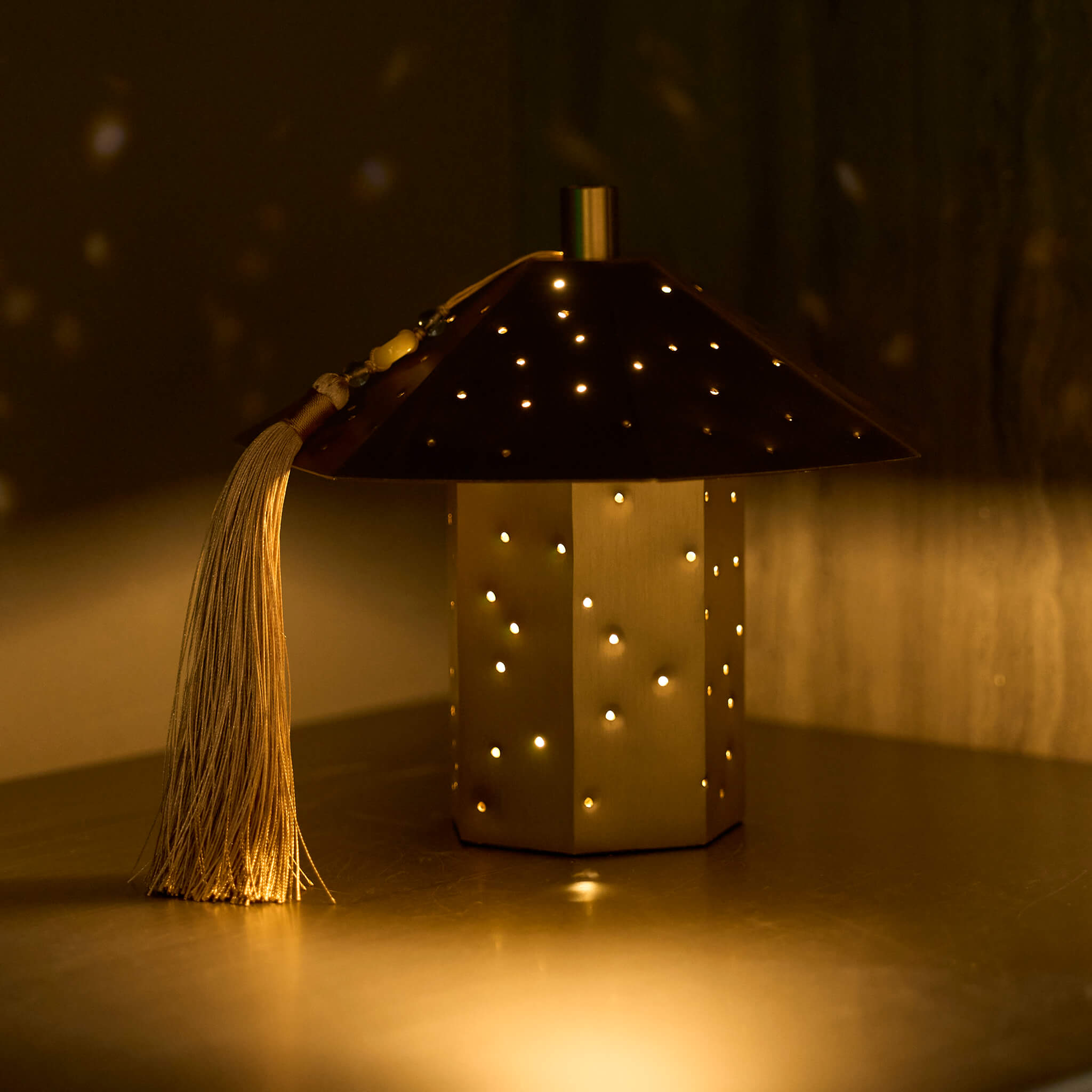Hammered brass ambient lamp casting a tranquil starry sky effect in a dark minimalist bedroom aesthetic.