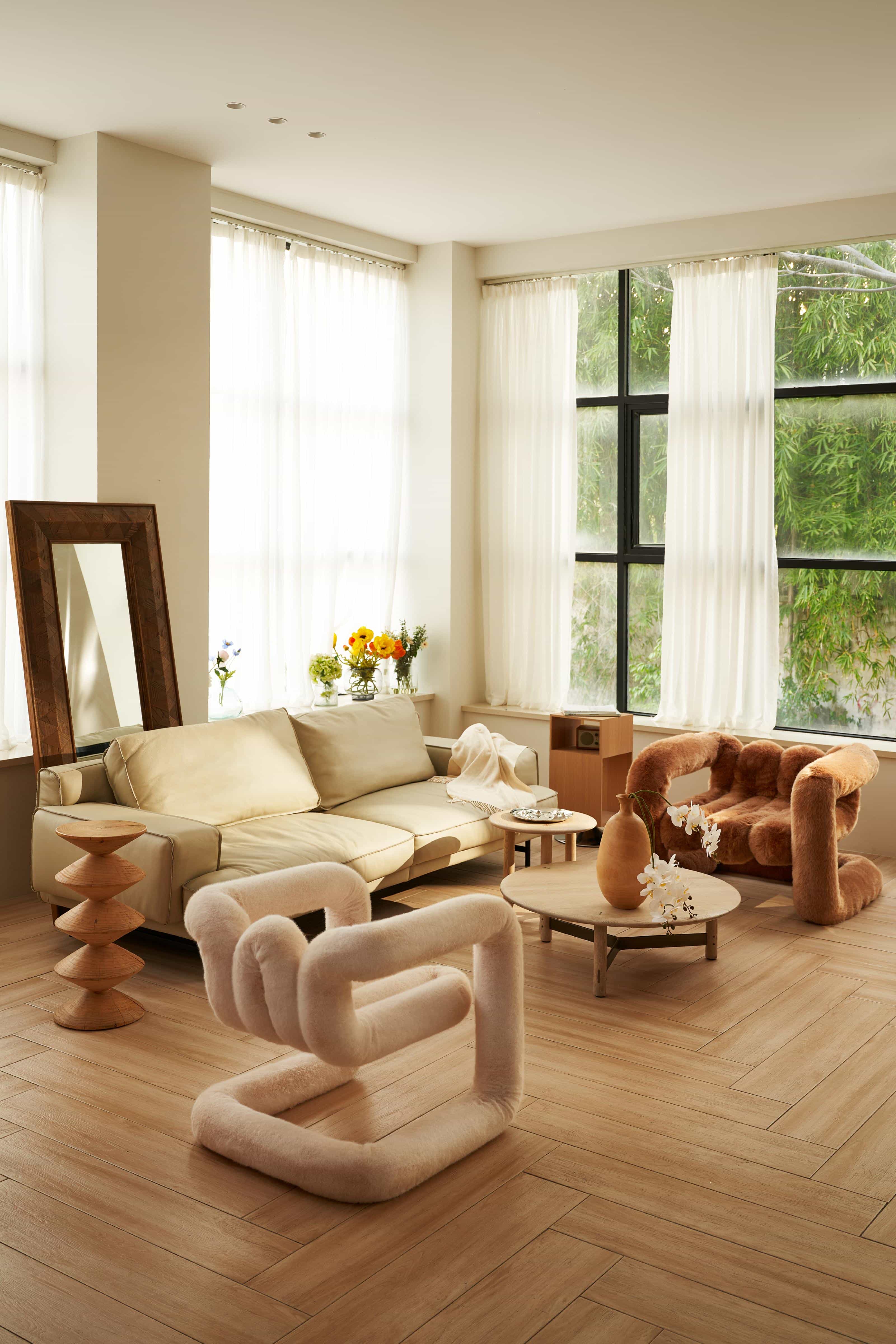 Contemporary sunlit living room featuring designer boucle seating, a beige sofa and sculptural wooden tables.