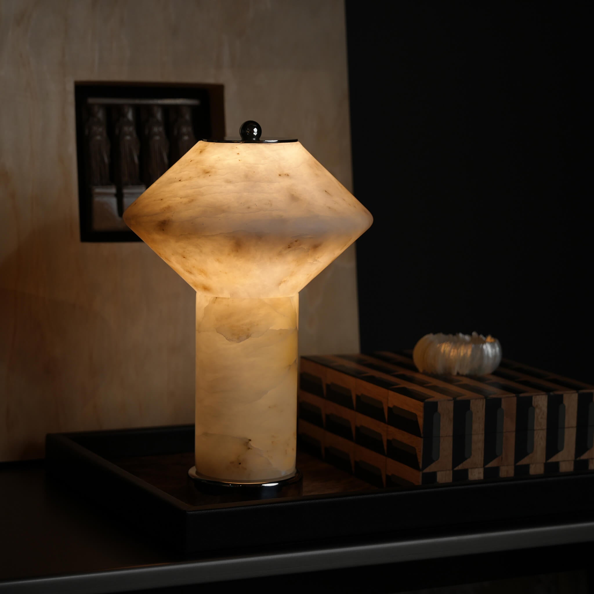 The cordless alabaster table lamp illuminated, casting a warm, translucent ambient glow on a dark, luxurious living room tray.