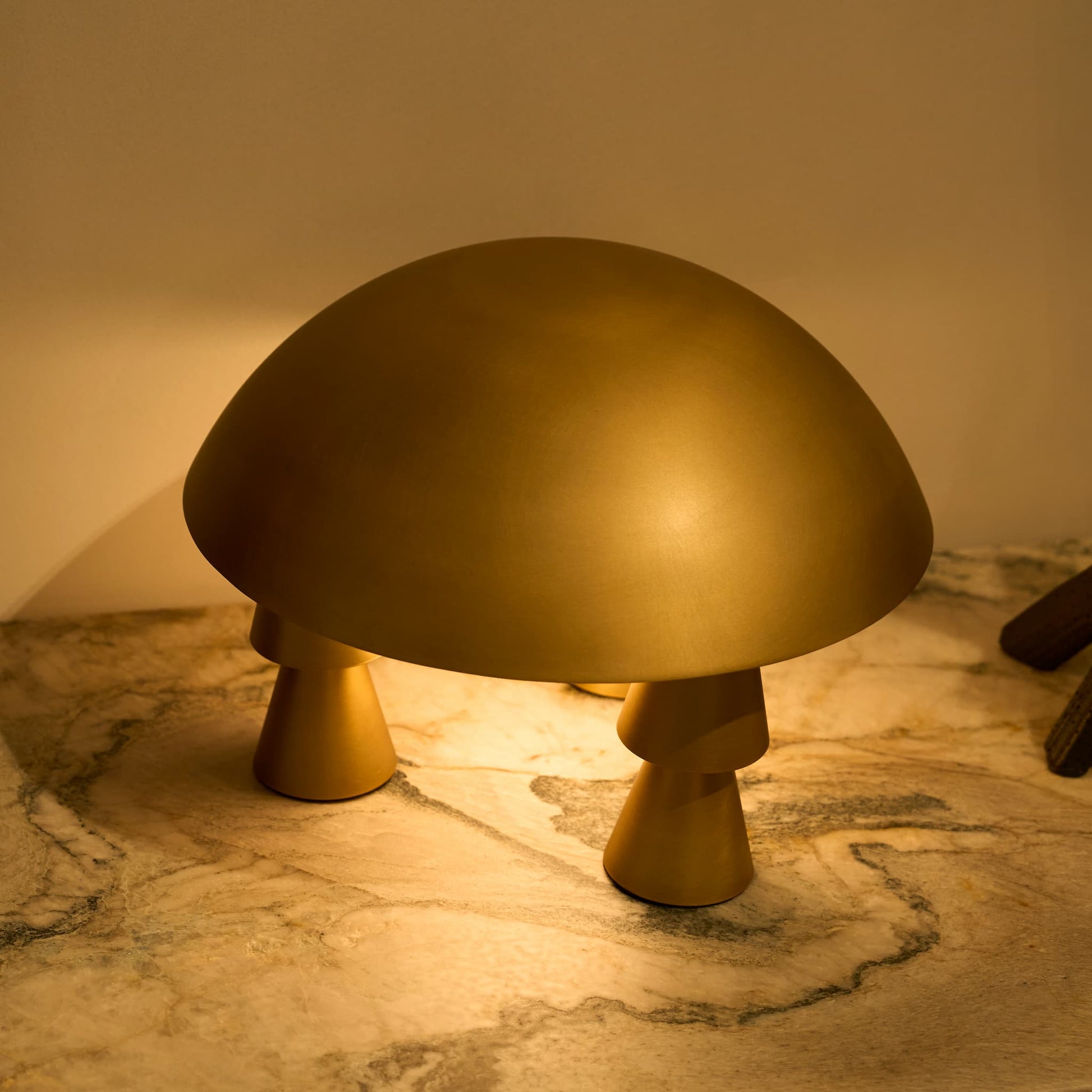 Close-up of the elegant diffused light shining downwards onto the lamp's textured brass geometric legs on a marble surface