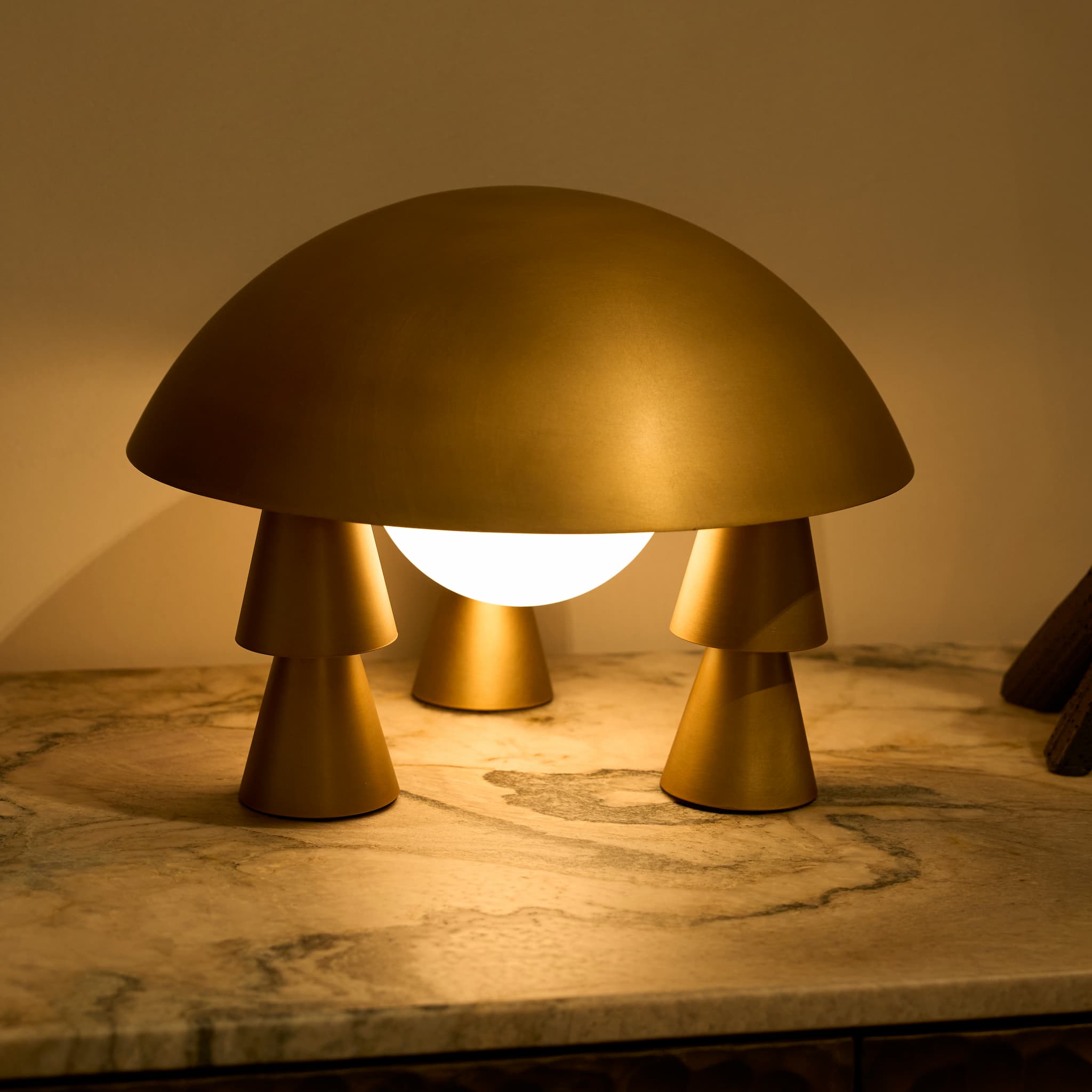 The rechargeable metal sculptural lamp casting a warm, soft ambient light on a marble side table in a dimly lit room
