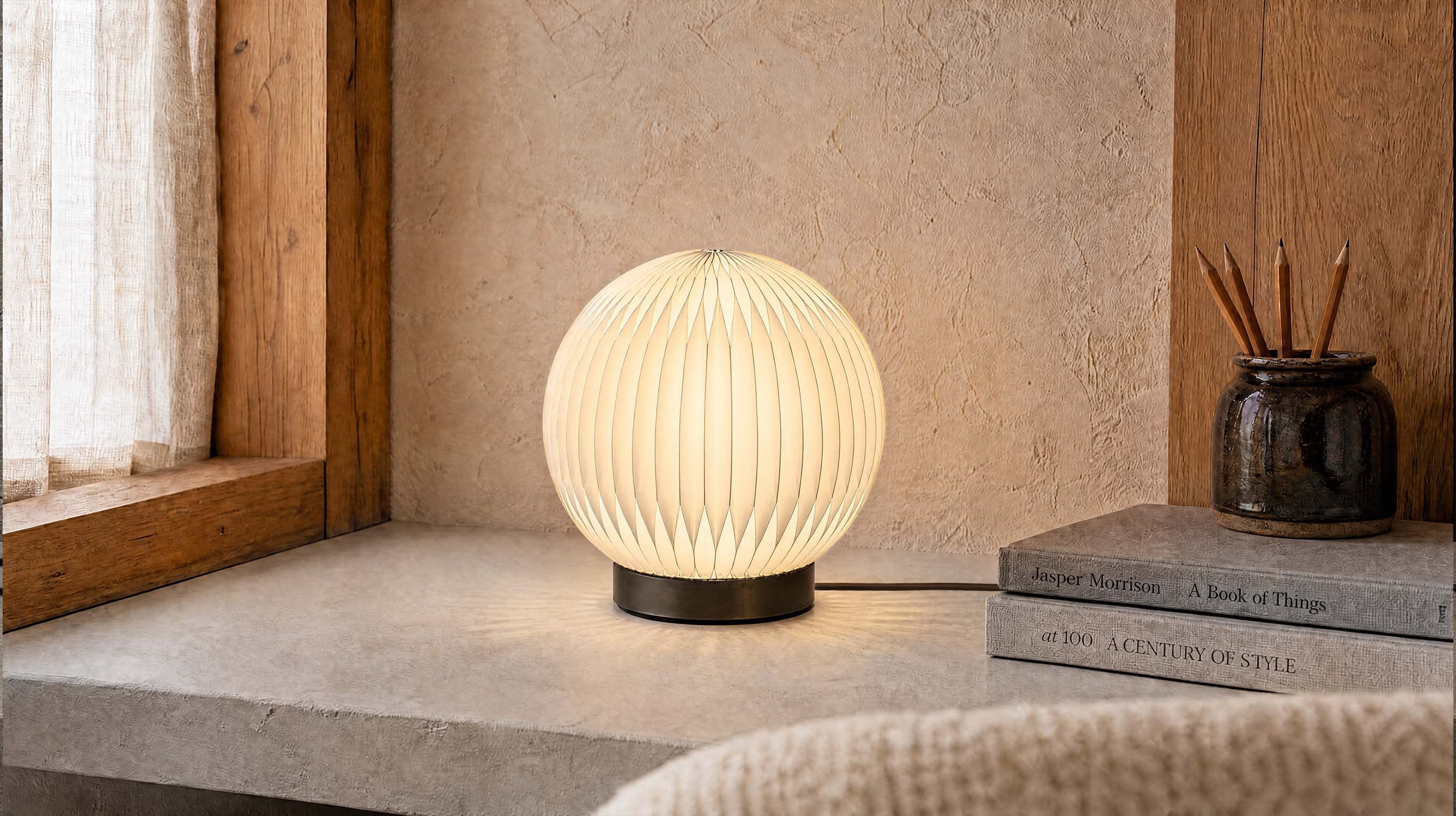 The artamore Crescent Moon Desk Lamp casting a gentle, warm glow through its soft accordion-paper shade in a modern minimalist setting.