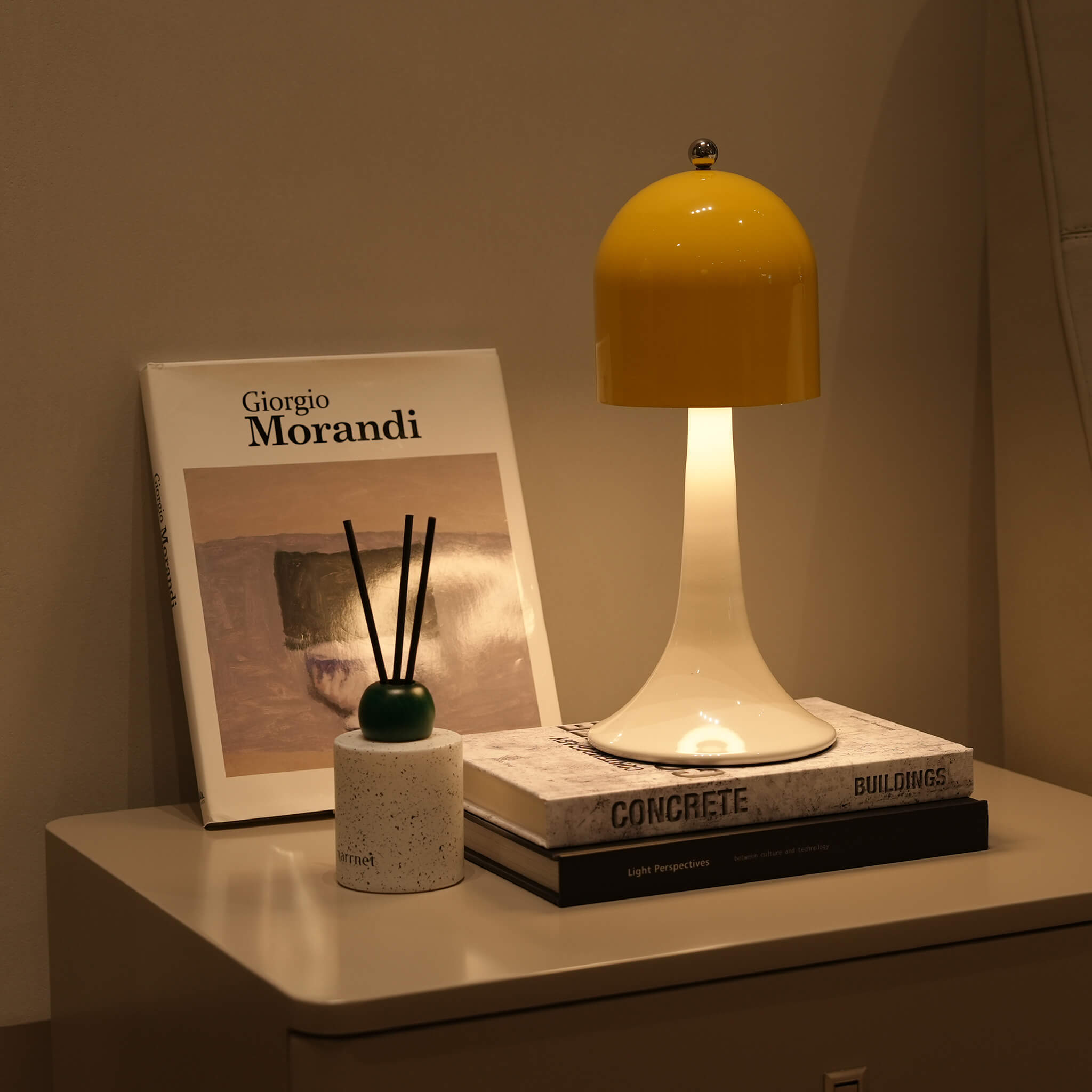 A vintage bell silhouette lamp in vibrant yellow illuminating a modern nightstand beside a Giorgio Morandi art book