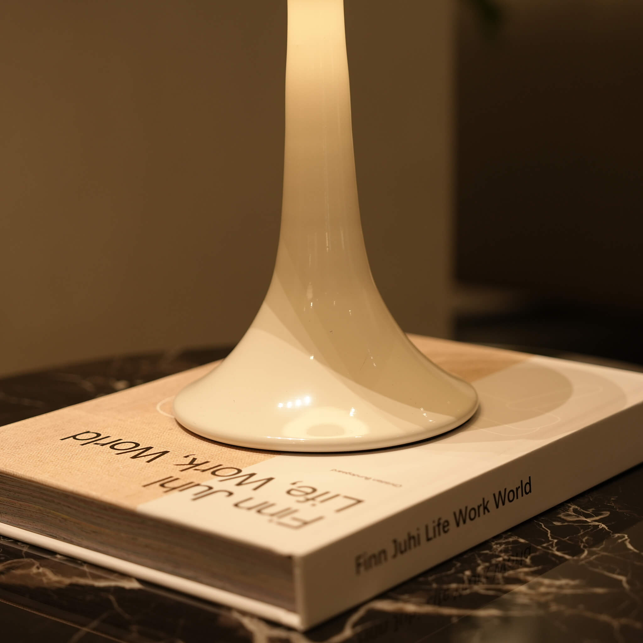 Detail shot of the smooth, curved metal base of the portable nightstand light resting elegantly on a coffee table book