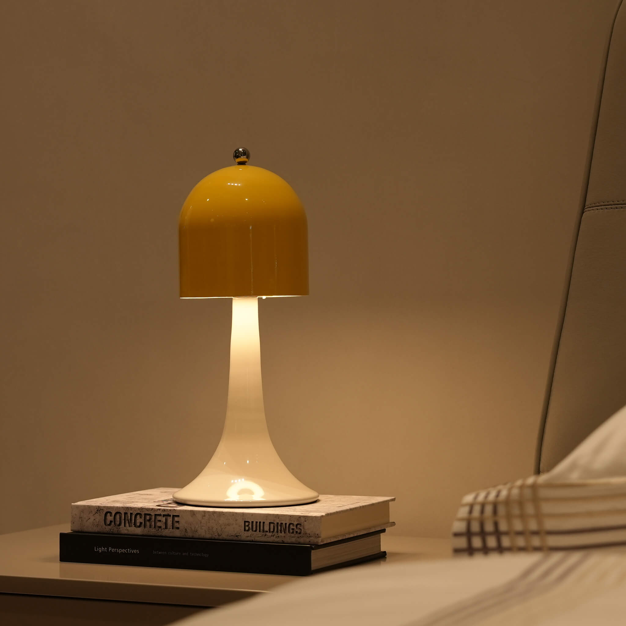 The Ardour Yellow dimmable bedside reading lamp placed gracefully on stacked books in a cozy, warm-toned bedroom setting