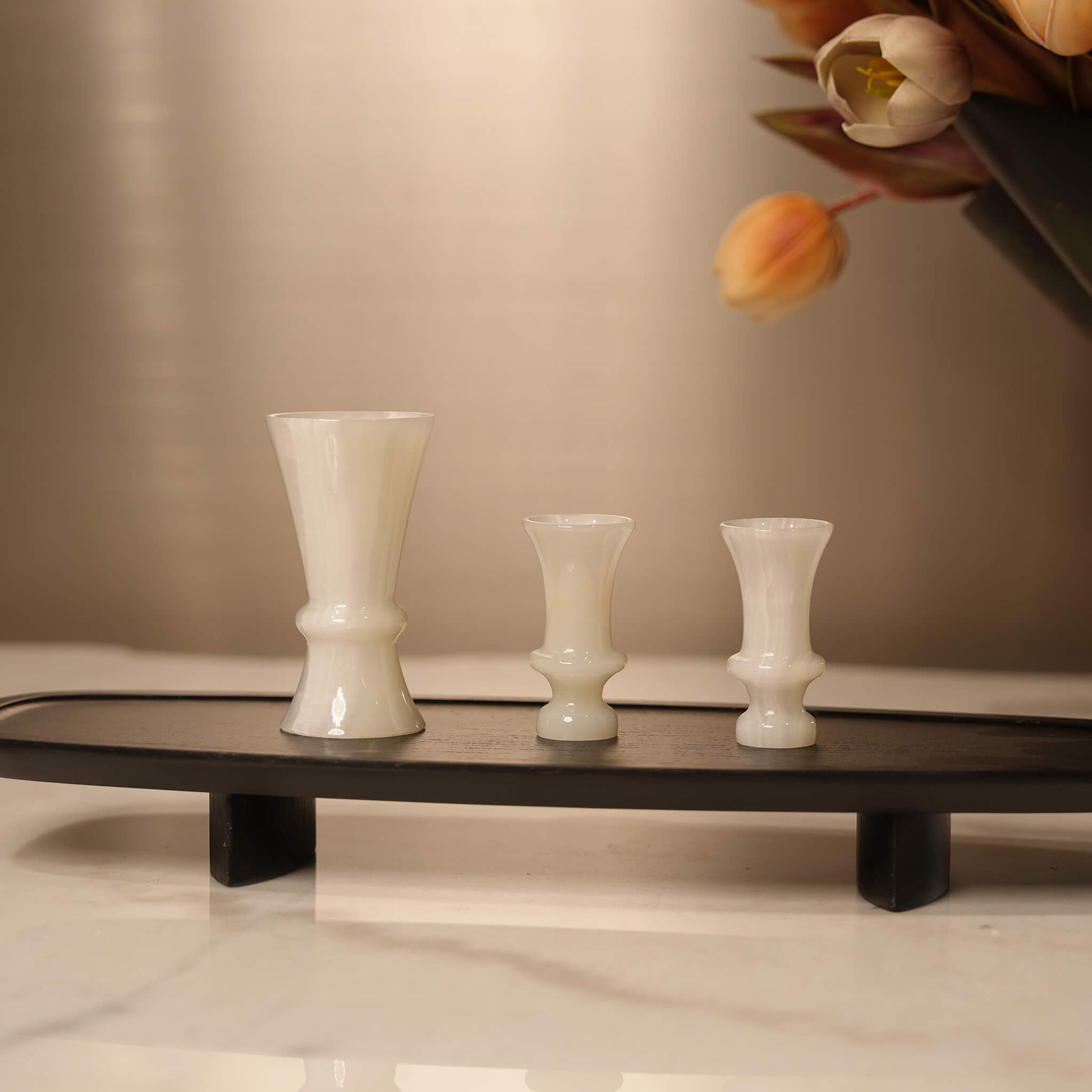 Black elongated wooden tray styling a marble console table, holding three white onyx cups alongside a floral arrangement
