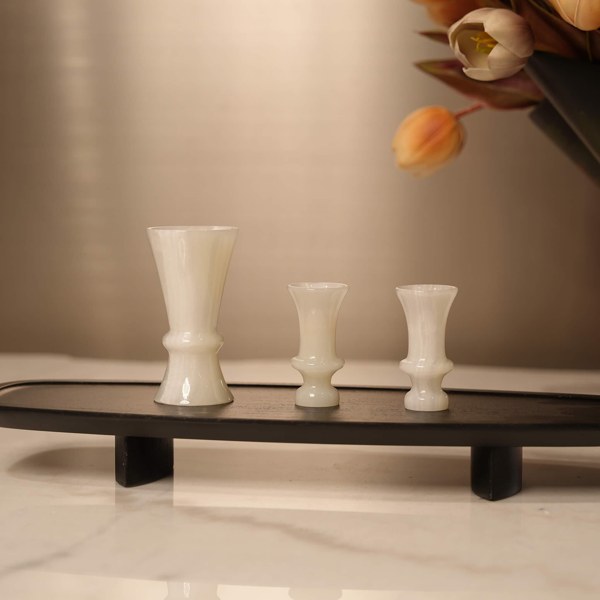 Black elongated wooden tray styling a marble console table, holding three white onyx cups alongside a floral arrangement
