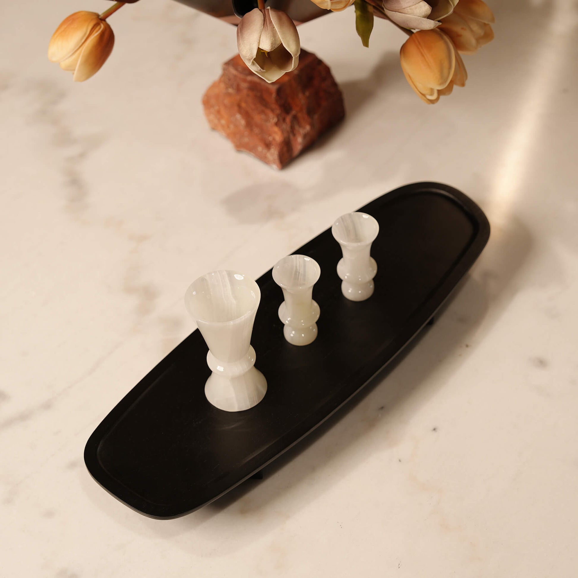 High-angle view of an elegantly elongated black wooden tray bathed in warm light on a white marble surface
