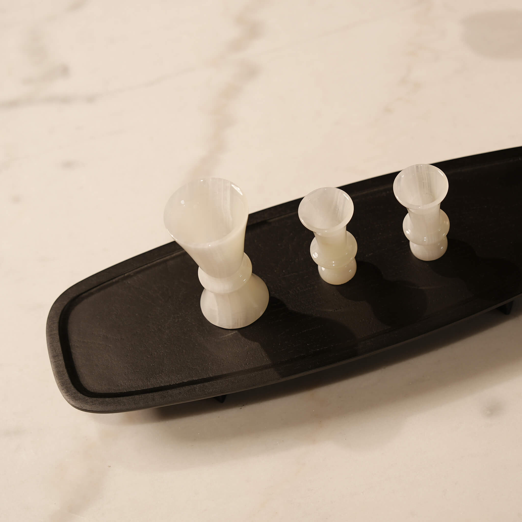 Top-down angled lifestyle shot of a long black wooden tray displaying decorative white marble cups
