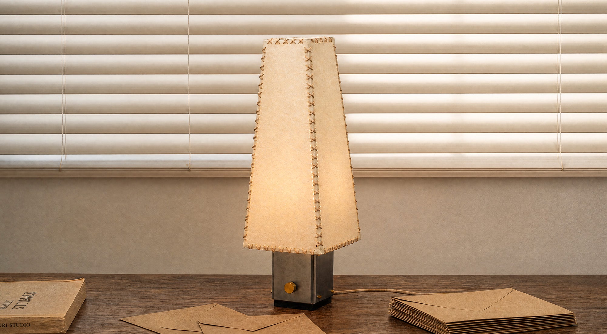 The artamore handmade parchment letter lamp emits a soft, warm glow, showcasing its wabi-sabi aesthetic and naturally wrinkled texture in a modern minimalist setting.