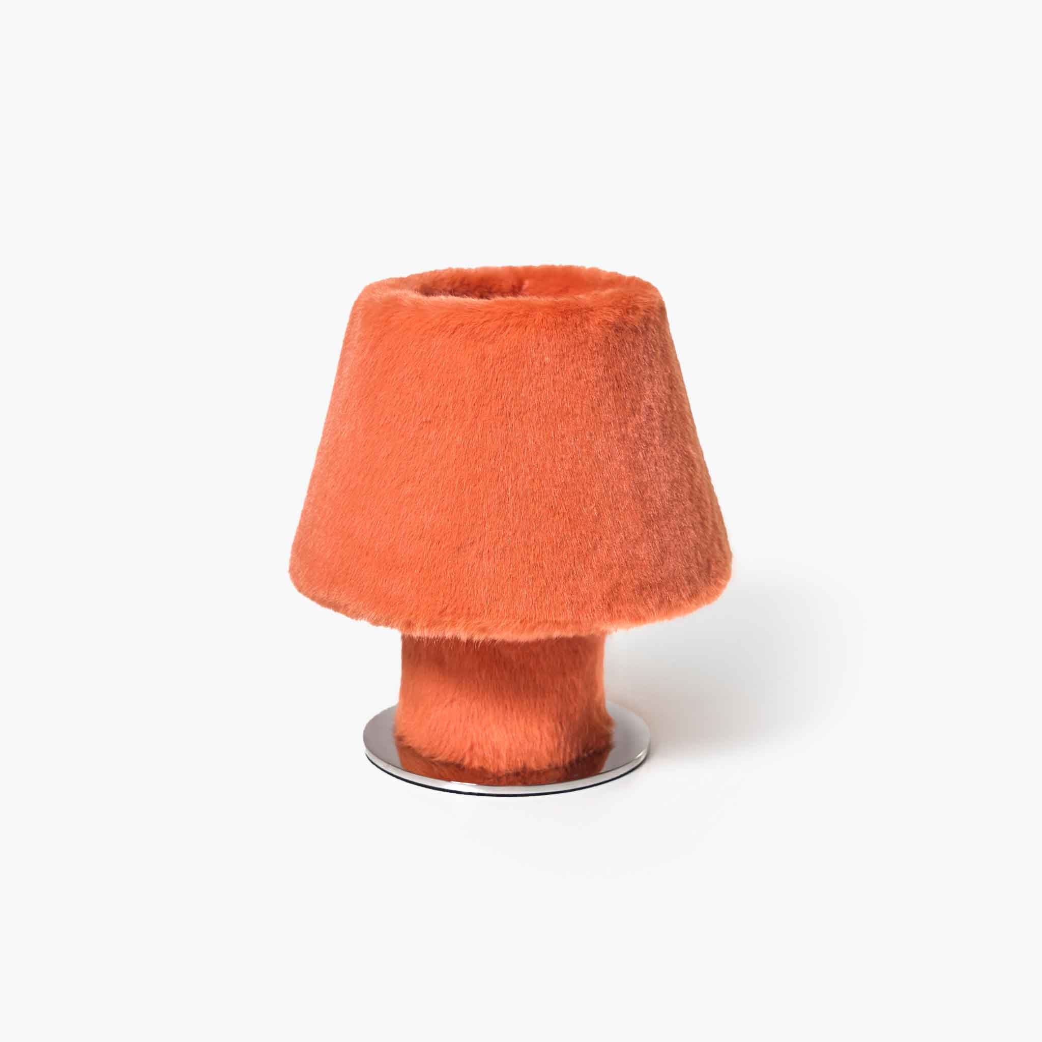 Exclusive orange plush faux fur table lamp radiating a comforting ambient glow on a modern nightstand.