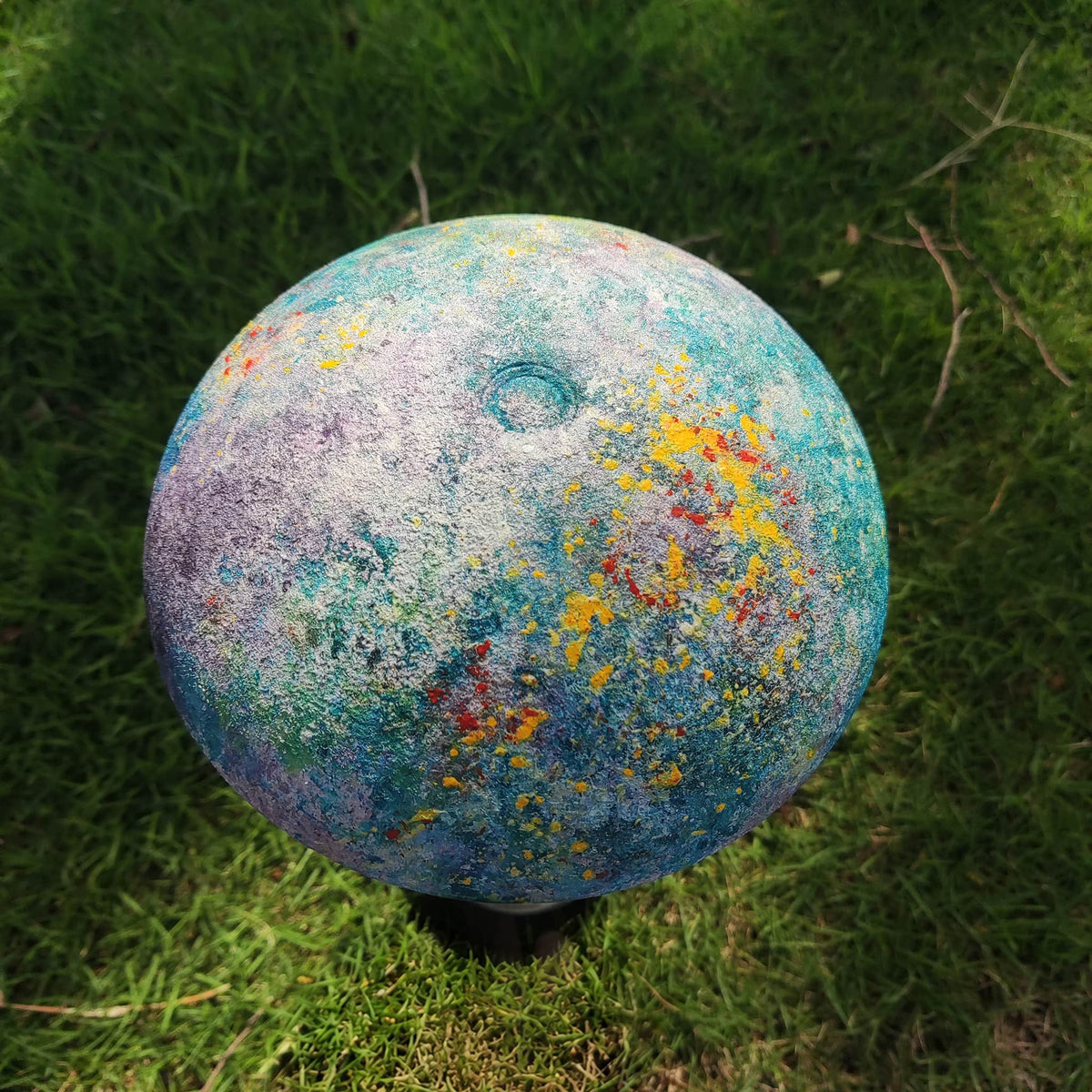 Close-up of a colorful abstract hand-painted Relax-W lamp shade displayed outdoors on green grass.
