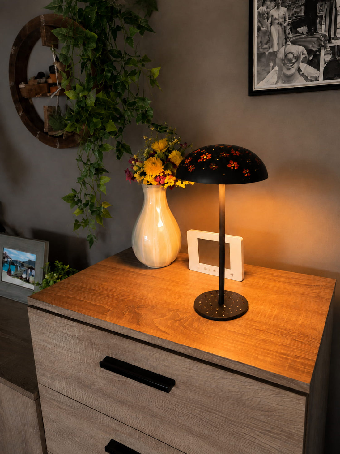 Black floral-painted Relax-W DIY portable table lamp creating warm ambient light on a wooden sideboard.
