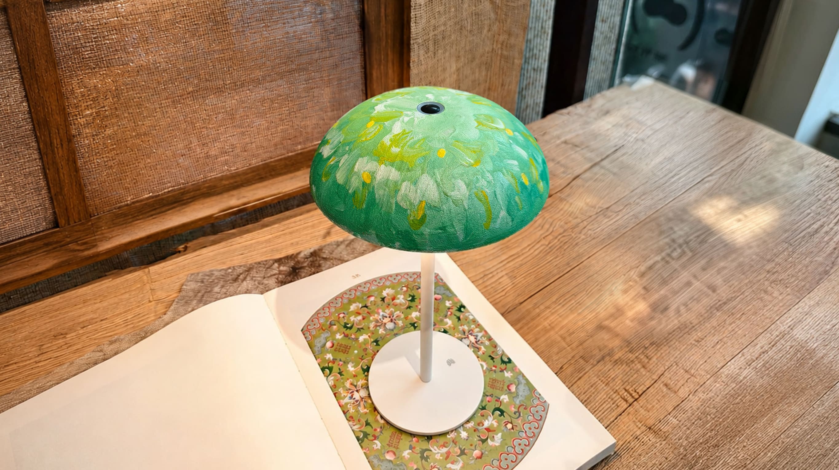 Green floral hand-painted Relax-W DIY portable table lamp with a white base styled on an open art book and wooden table.
