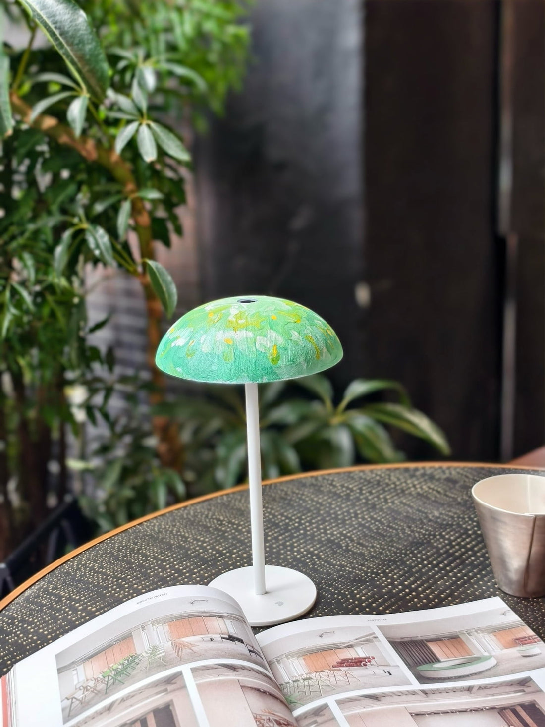 Green hand-painted Relax-W portable table lamp displayed on a dining table with books and indoor plants.