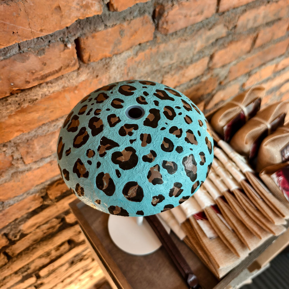 Turquoise leopard-print Relax-W portable DIY table lamp with a white base styled beside a brick wall and woven chair.