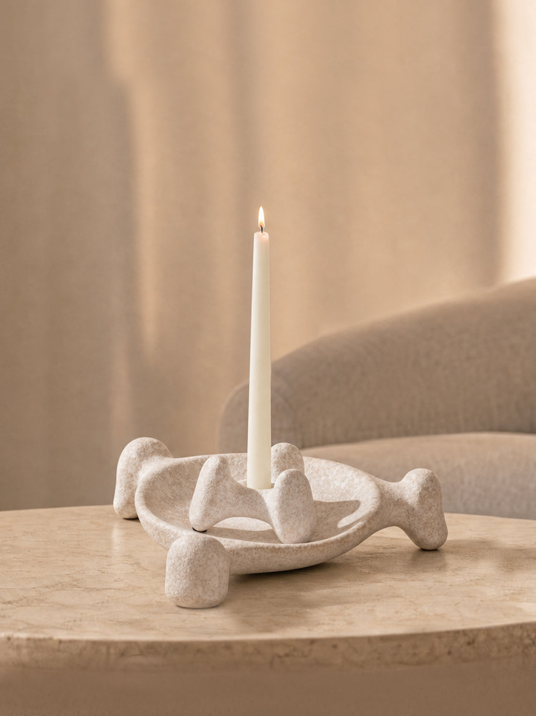 Sculptural candle holder with a white taper candle styled on a warm neutral stone table.