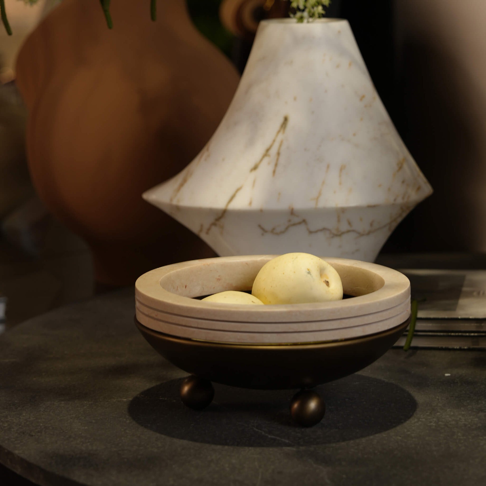 Antique bronze and travertine decorative bowl placed on a modern entryway table next to a geometric marble vase