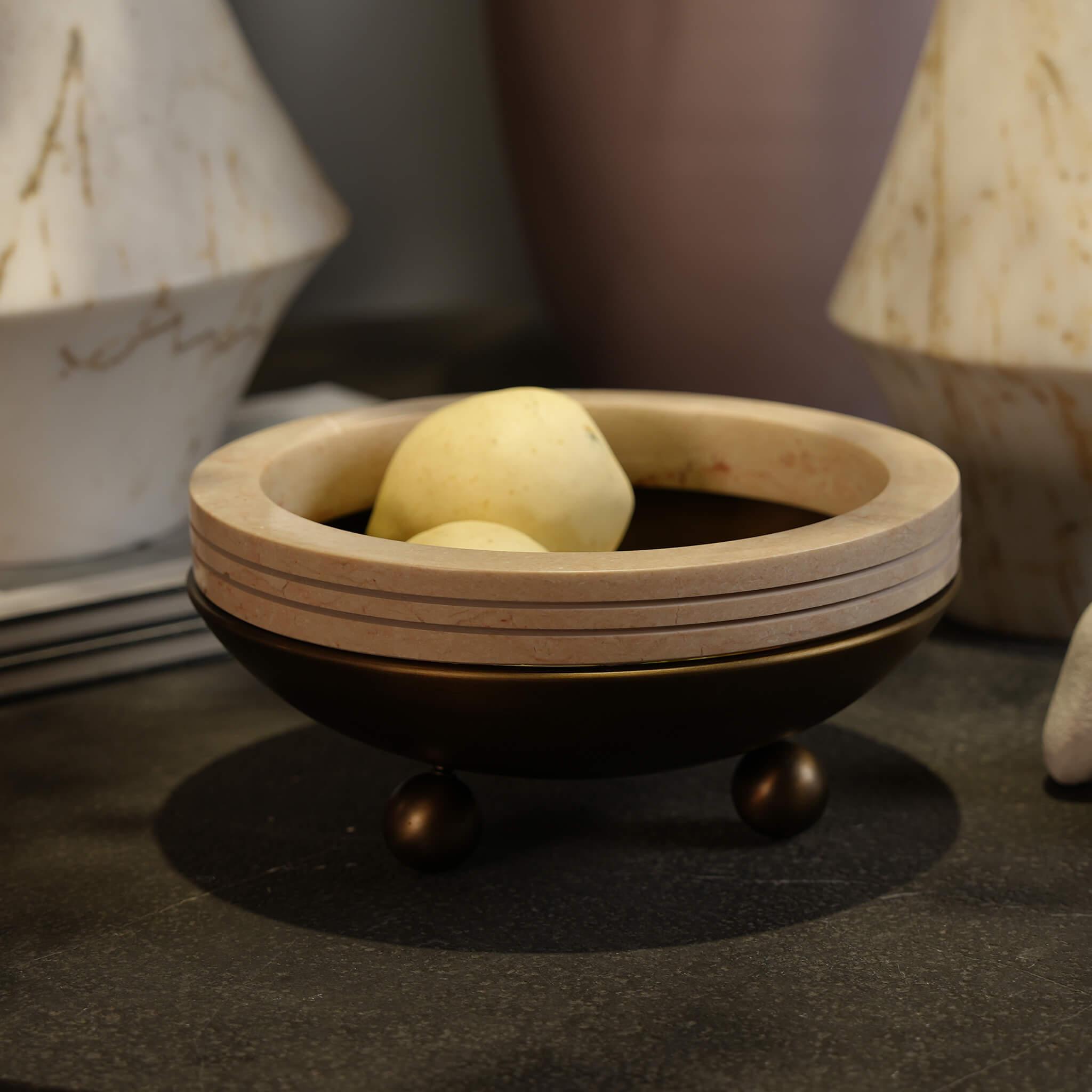 Natural travertine decorative bowl styled with fresh fruit on a dark stone coffee table, creating a sophisticated visual focal point