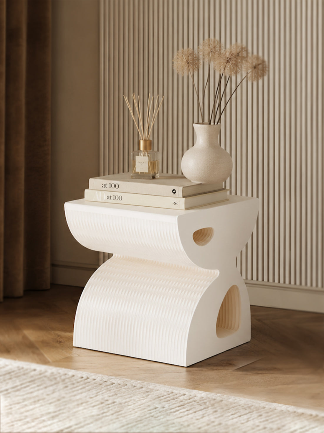 White sculptural side table styled with books, a reed diffuser and a ceramic vase in a modern interior.