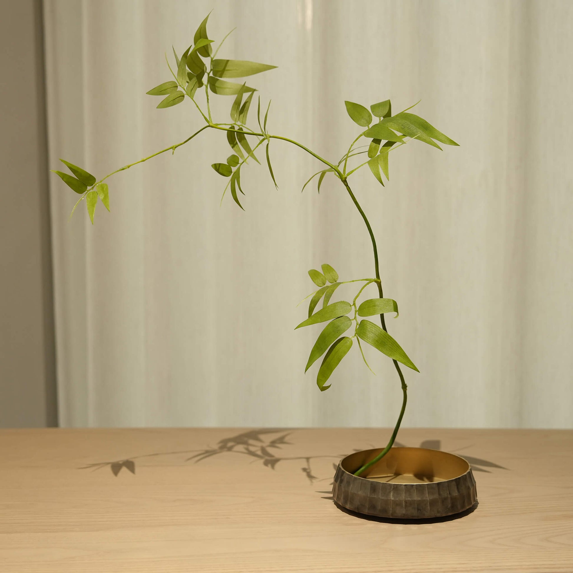 Zen-style Ikebana arrangement using the solid brass vessel, casting elegant shadows on a wooden table