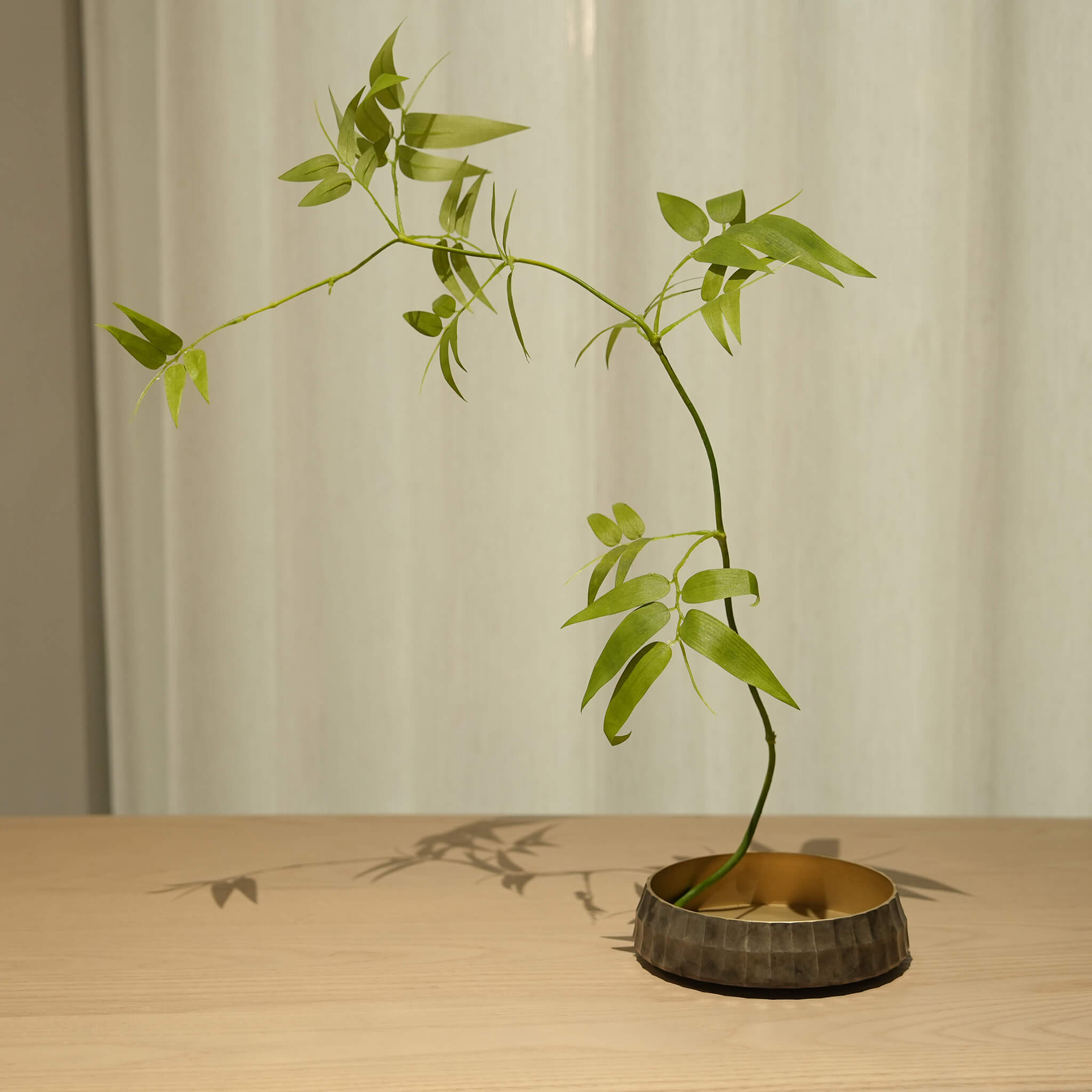 Zen-style Ikebana arrangement using the solid brass vessel, casting elegant shadows on a wooden table
