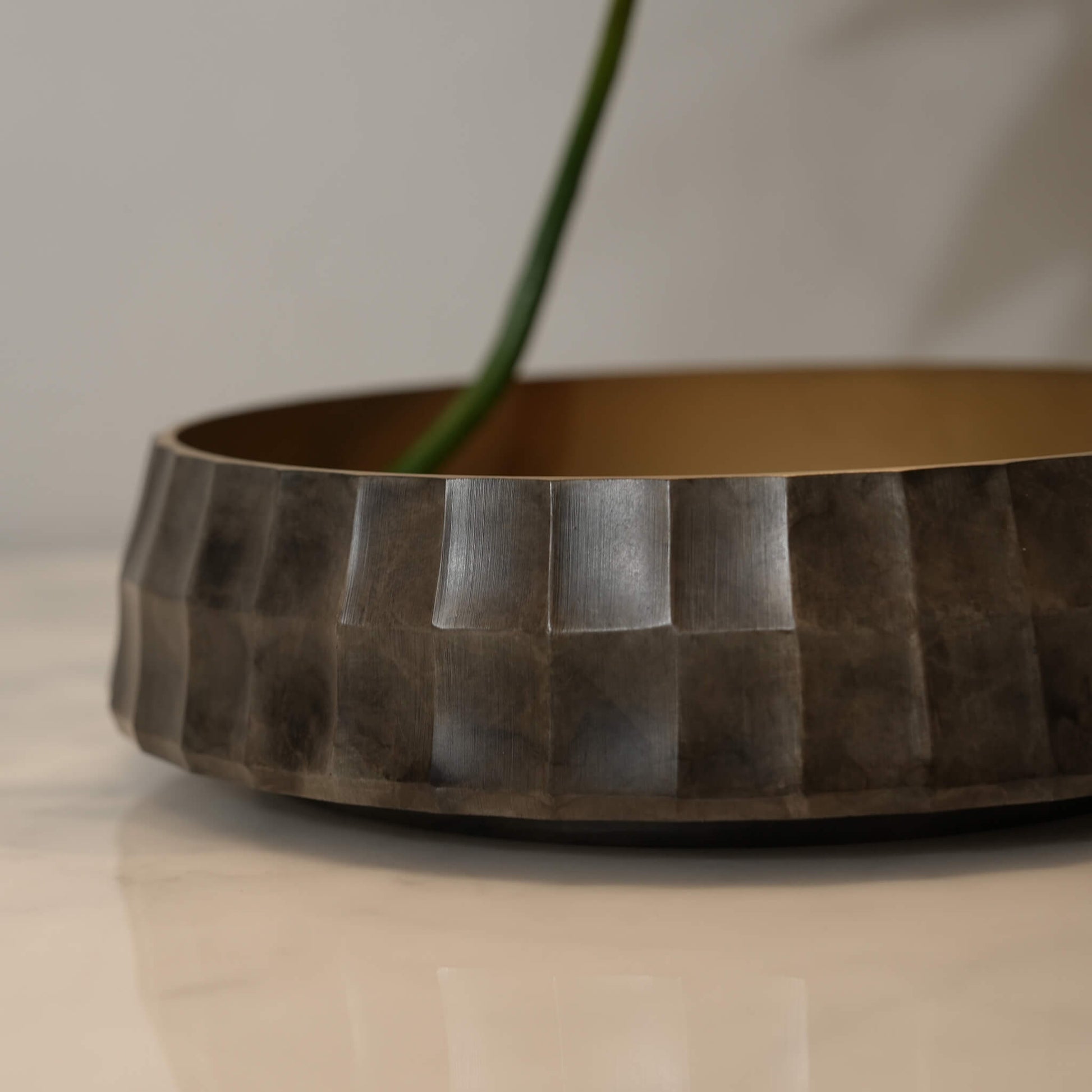 Close-up of a floral stem resting gracefully against the textured silver rim of the brass Ikebana bowl
