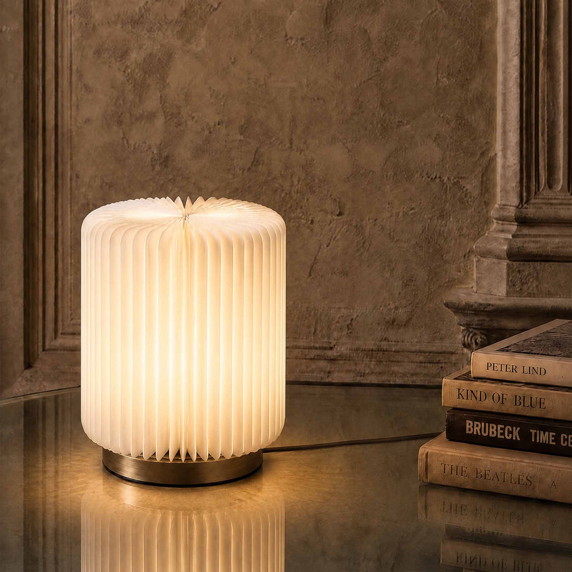 Bamboo Zen paper desk lamp with warm diffused light beside stacked books in a refined interior setting.