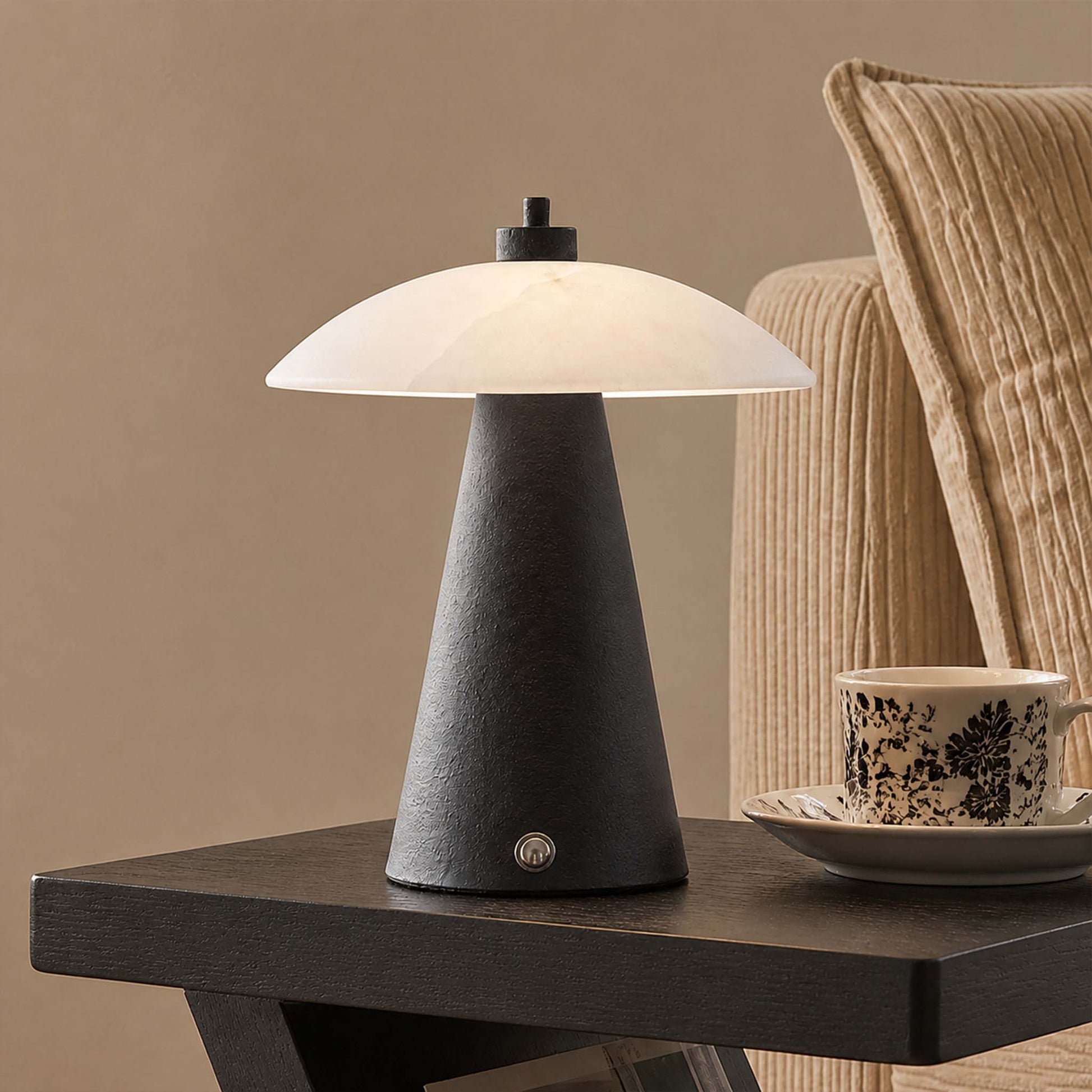 Black metal and marble table lamp with soft ambient light on a modern side table beside a coffee cup.