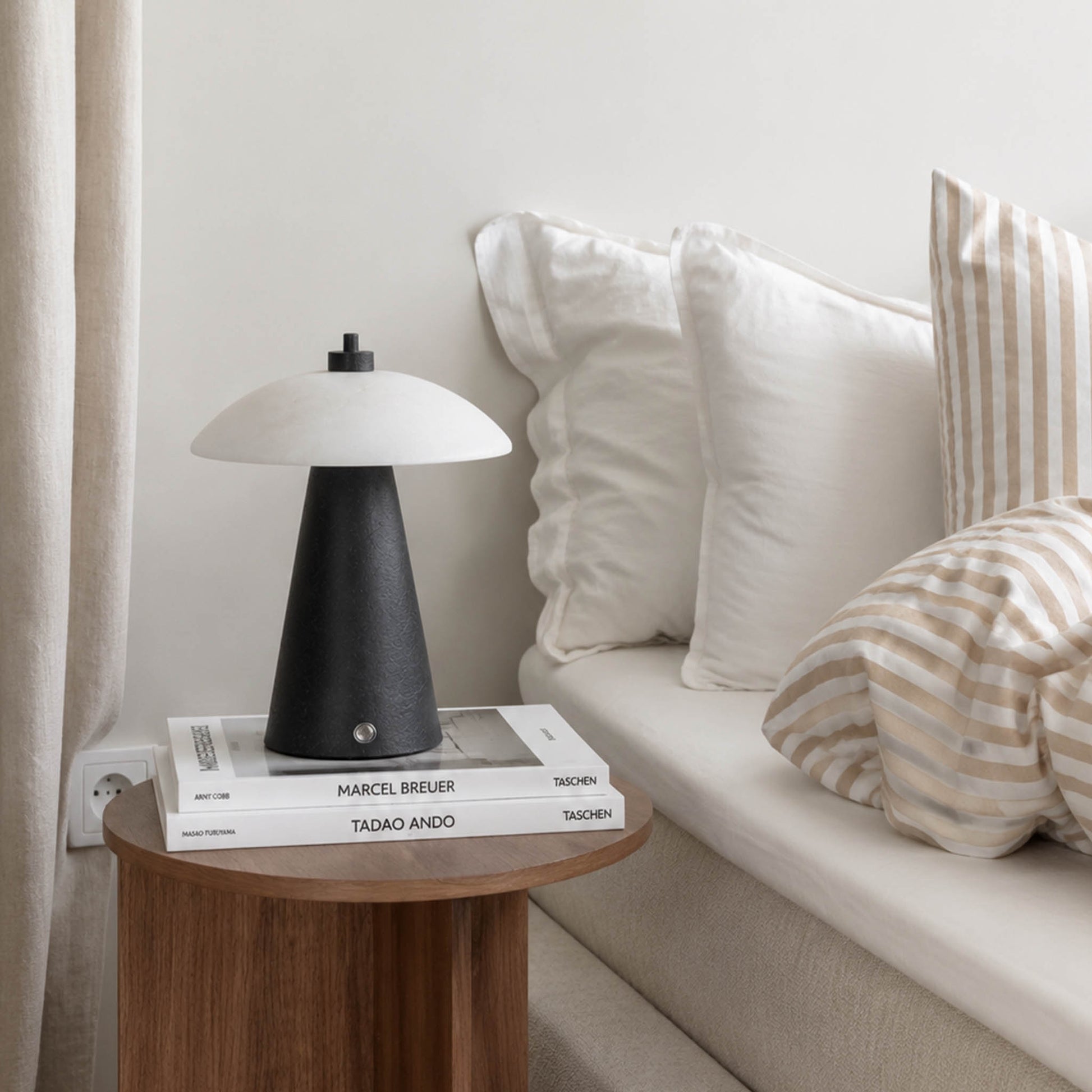 Black textured marble night light on a wooden bedside table with books beside a neutral bed.
