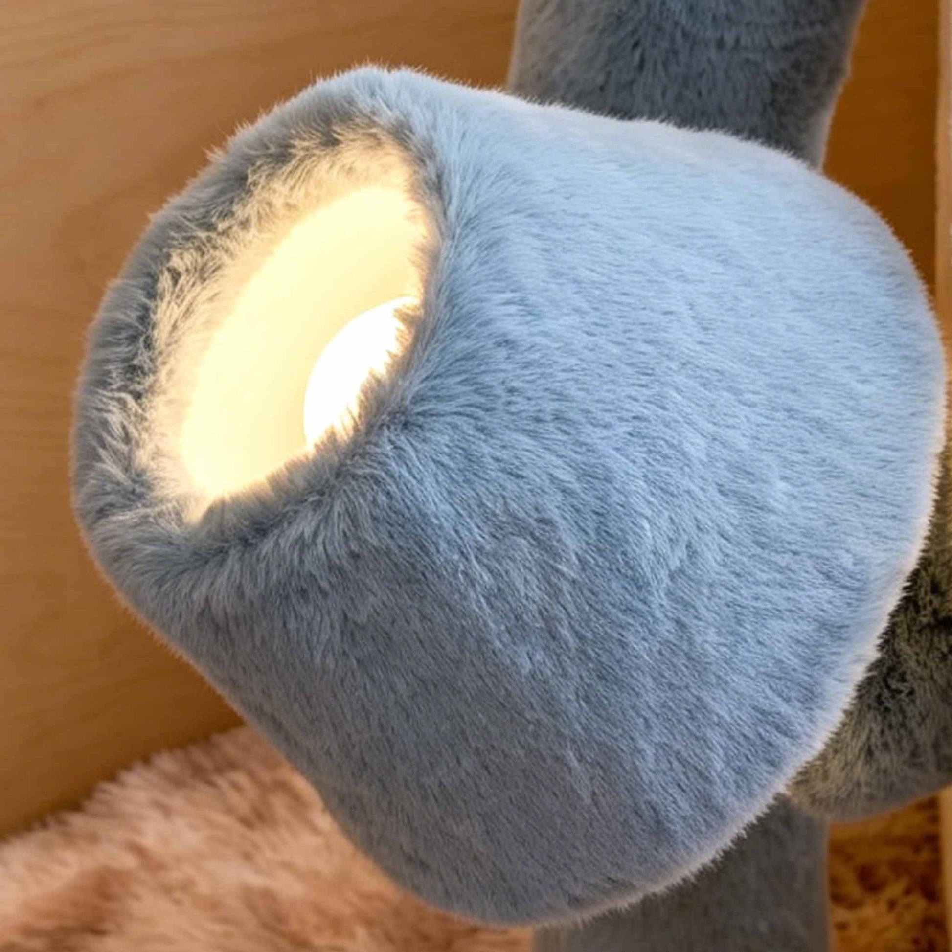 Close-up of a blue plush floor lamp shade with warm light glowing through the soft faux fur texture.