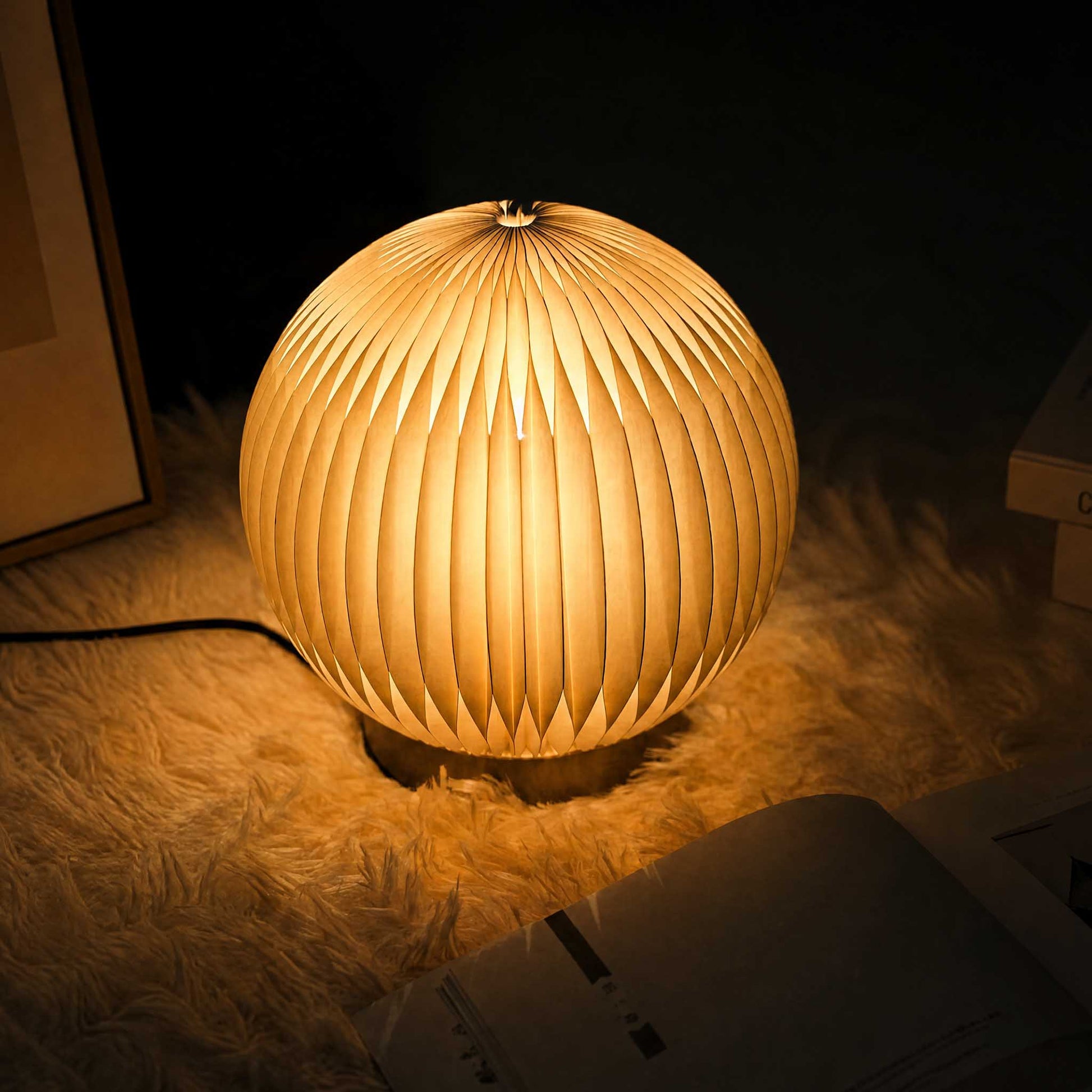 Crescent Moon paper desk lamp glowing softly on a textured rug for cozy bedside ambient lighting.