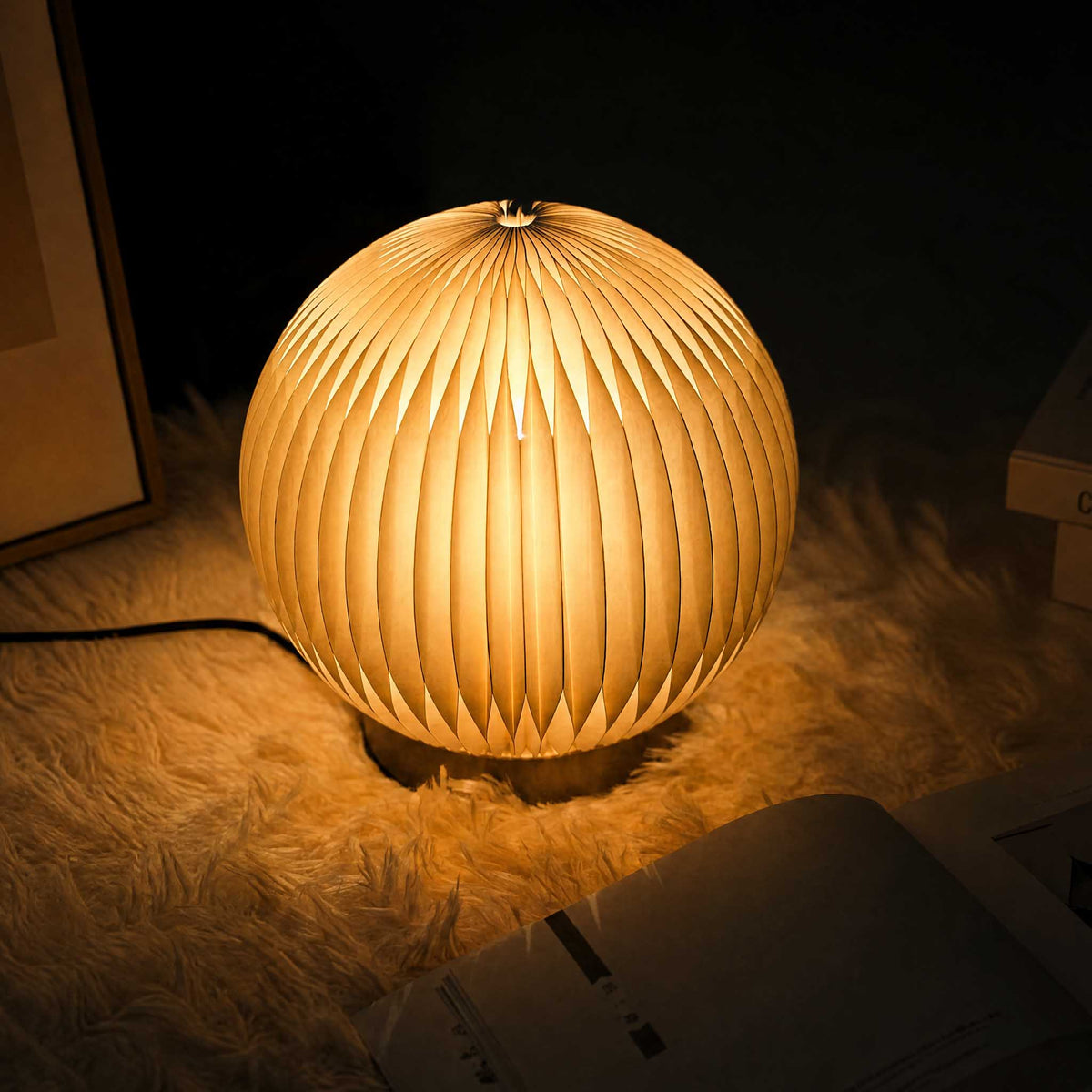 Crescent Moon paper desk lamp glowing softly on a textured rug for cozy bedside ambient lighting.
