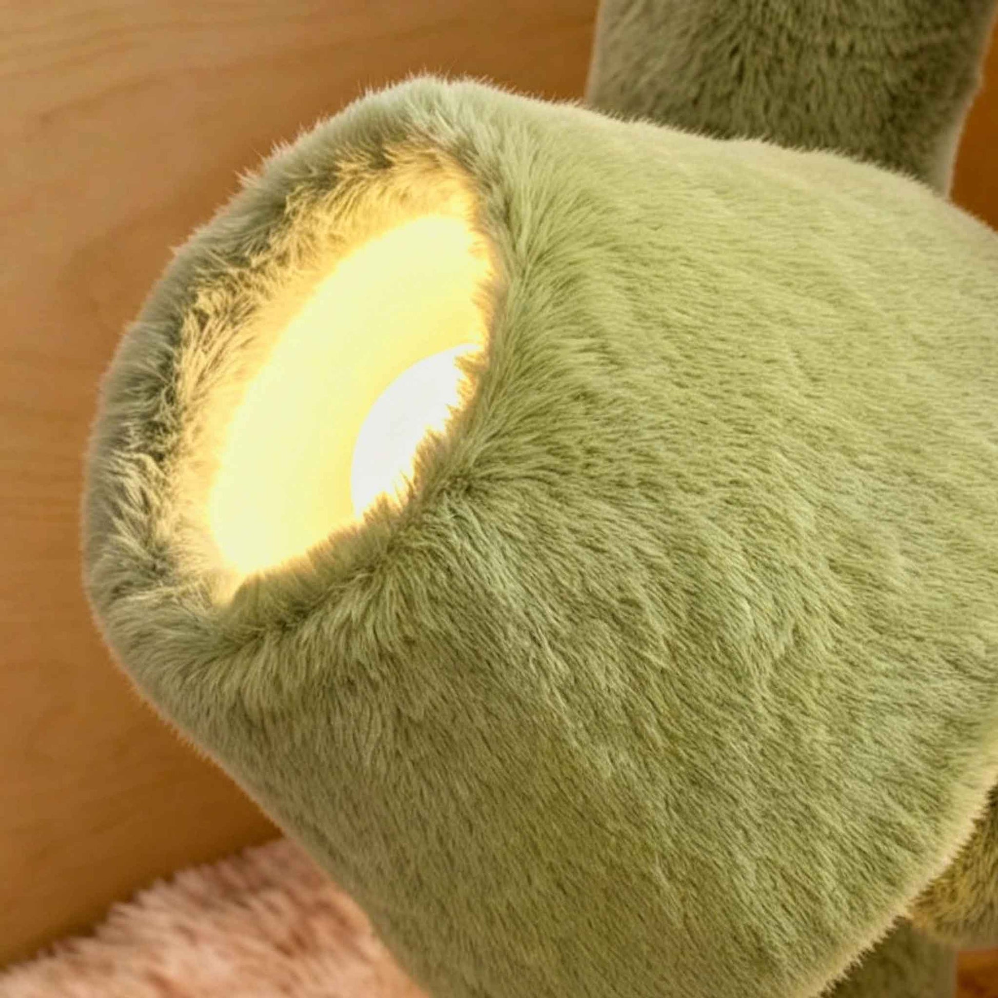 Close-up of a green plush floor lamp shade with warm light glowing through the soft faux fur texture.
