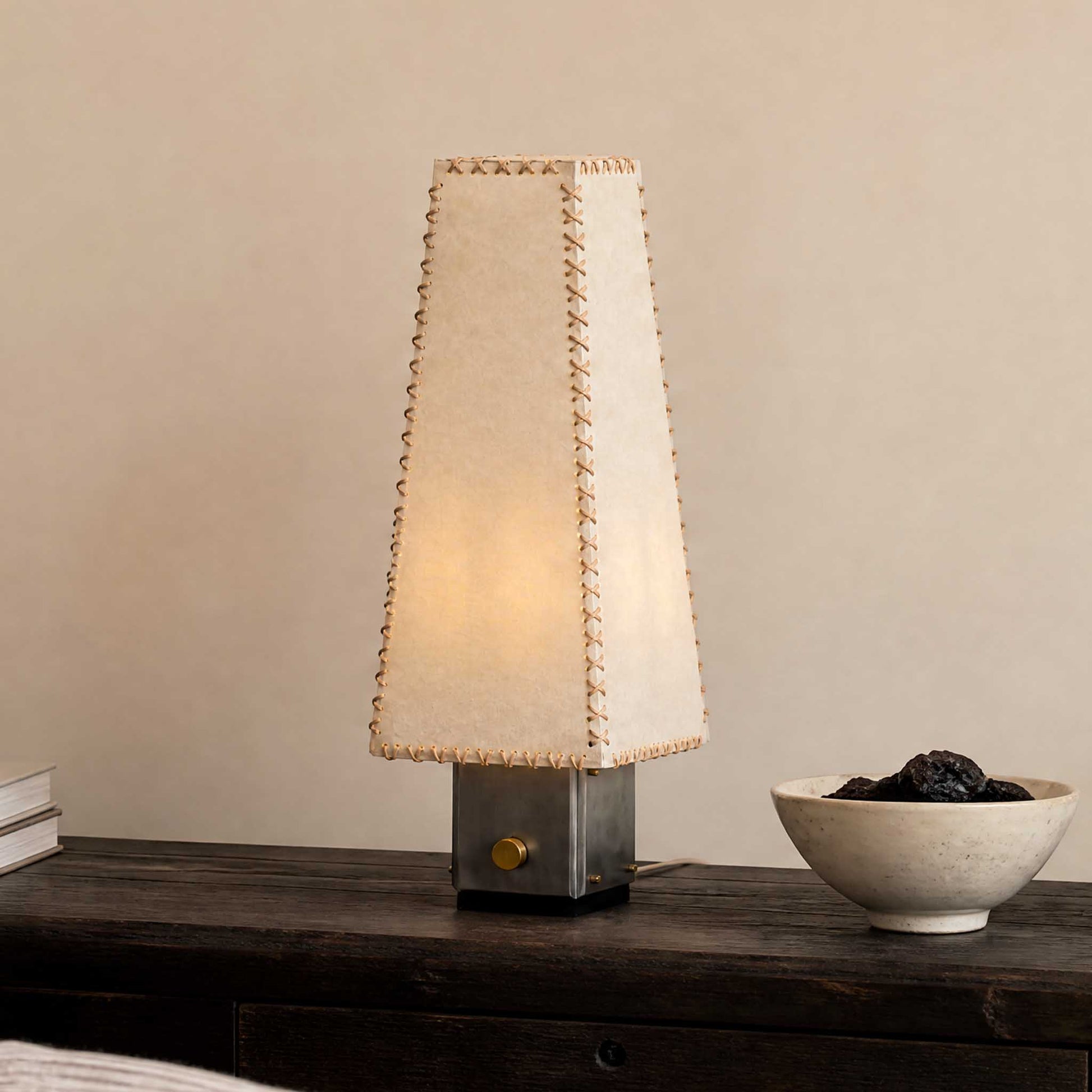 Handmade Parchment Letter Lamp on a dark wood sideboard with a soft glowing shade and minimalist ceramic bowl.