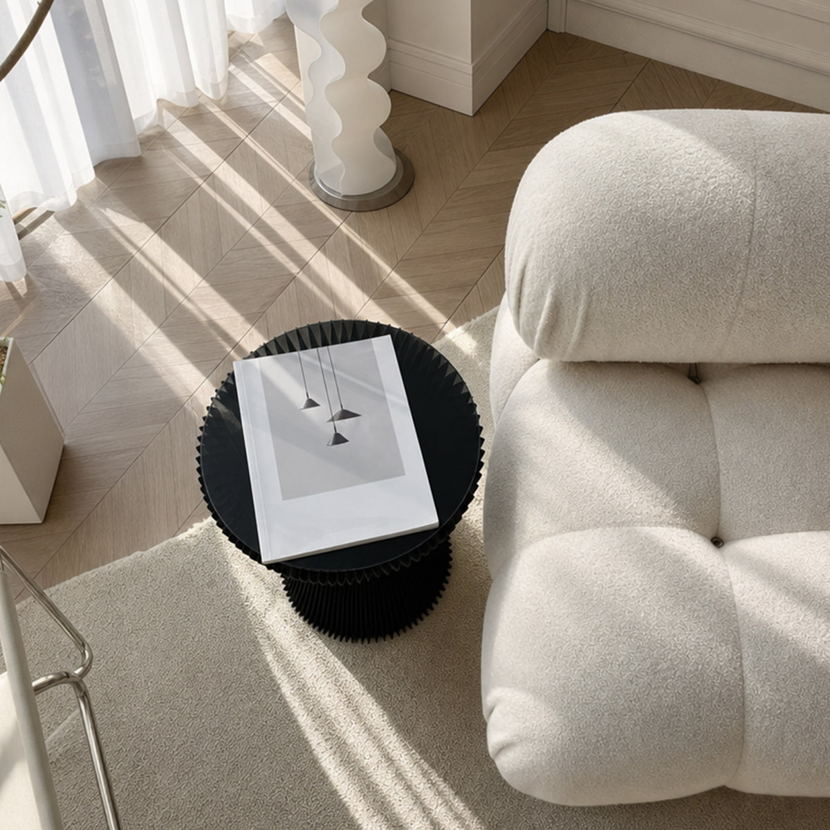 Top view of the black Little Black Dress Side Table beside a cream lounge chair with a book on the glass top