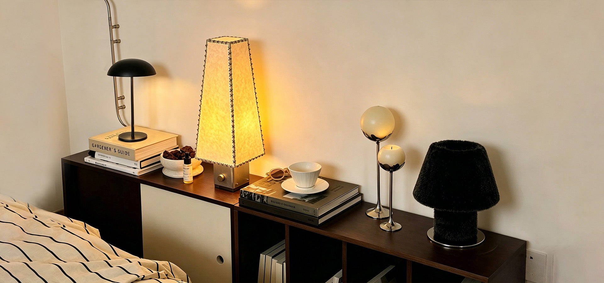 New collection of designer lighting and home decor styled on a dark wood console with table lamps, books, candles and sculptural accents.