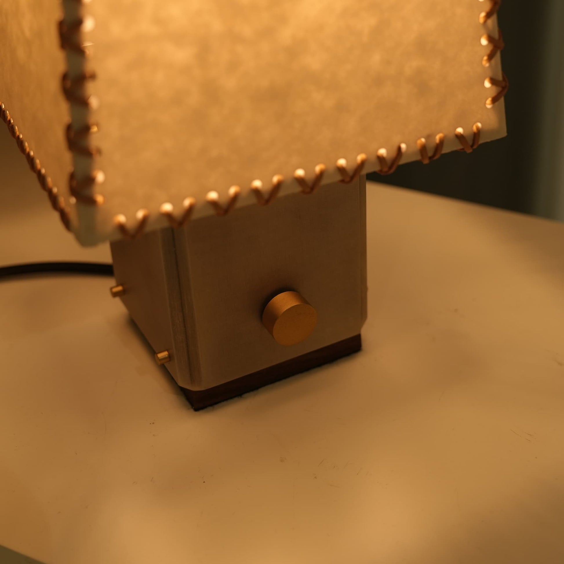 Close-up of the brass stepless dimmer knob on the parchment table lamp's metal base.