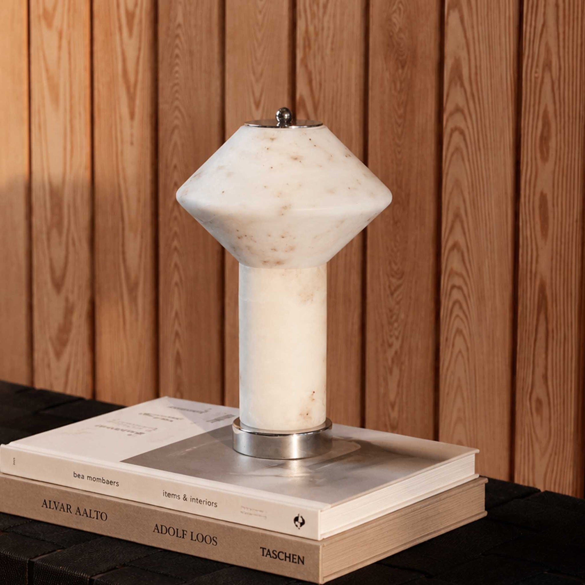 Rechargeable marble table lamp with warm ambient light on stacked books against a wooden interior wall.