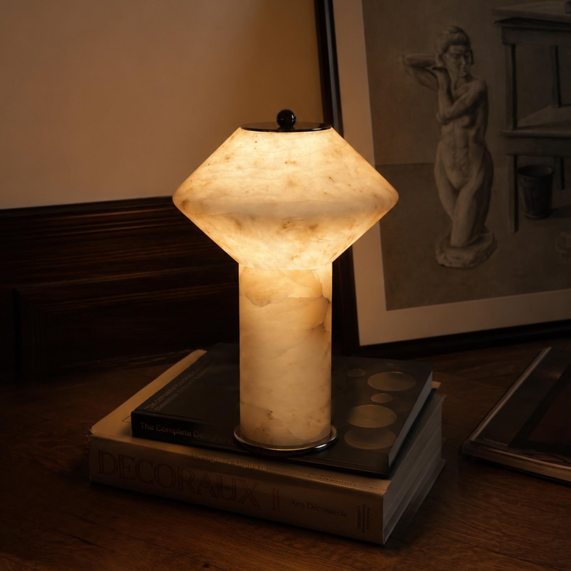 Rechargeable marble table lamp glowing warmly on books beside framed artwork in a calm evening interior.