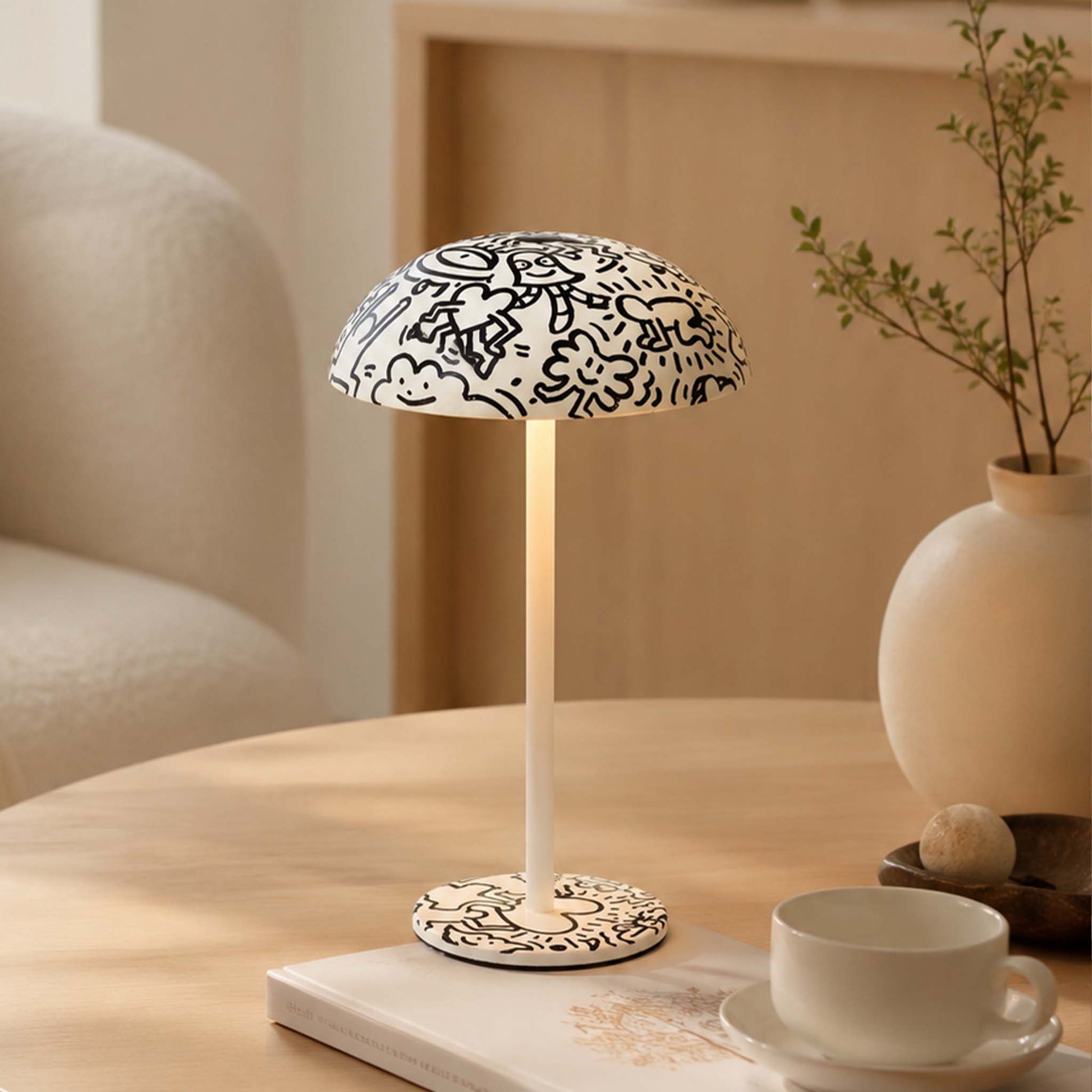 Black and white doodle painted table lamp with warm light on a coffee table in a cozy modern interior.