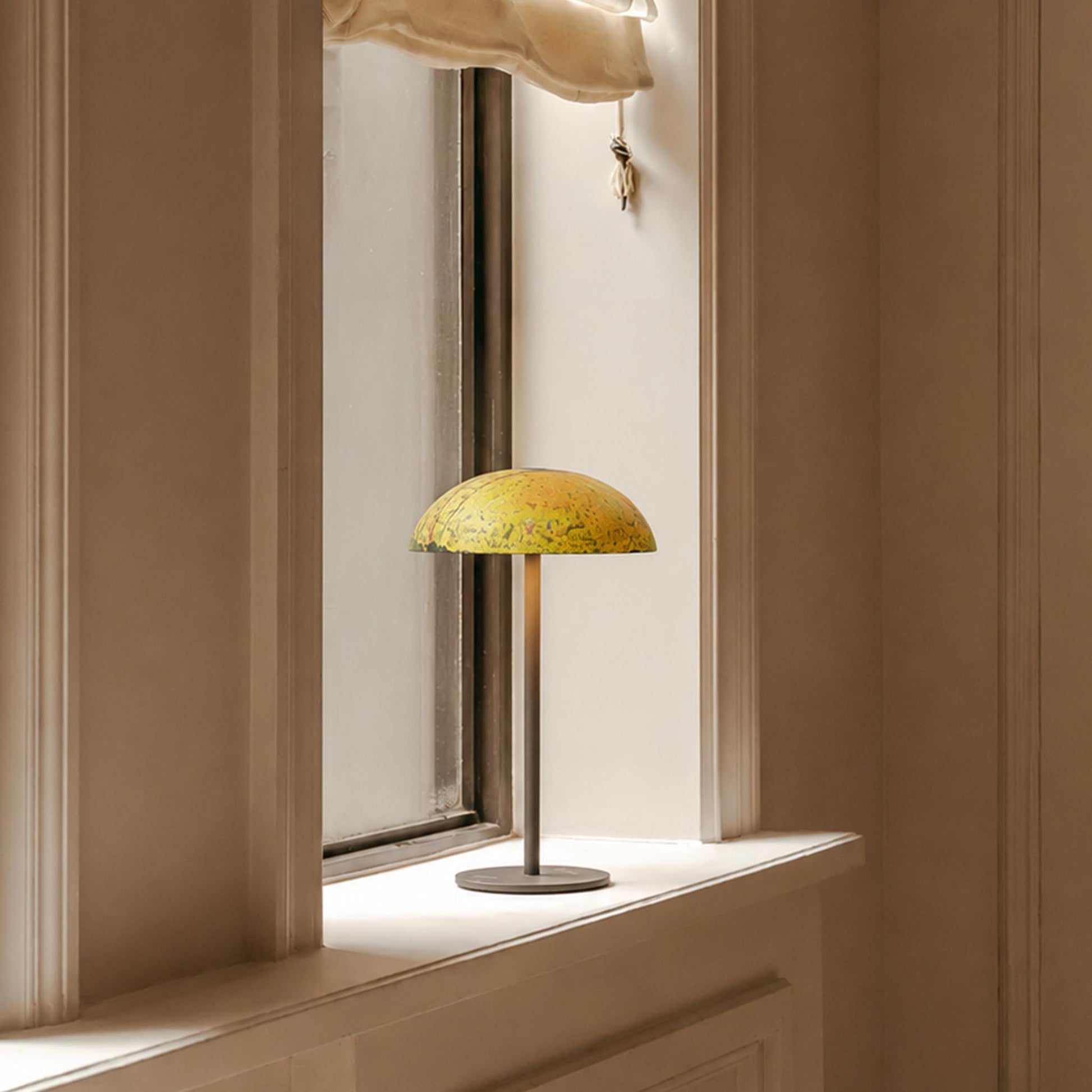 Yellow hand-painted Relax-W table lamp on a window sill with soft ambient light in a warm interior.