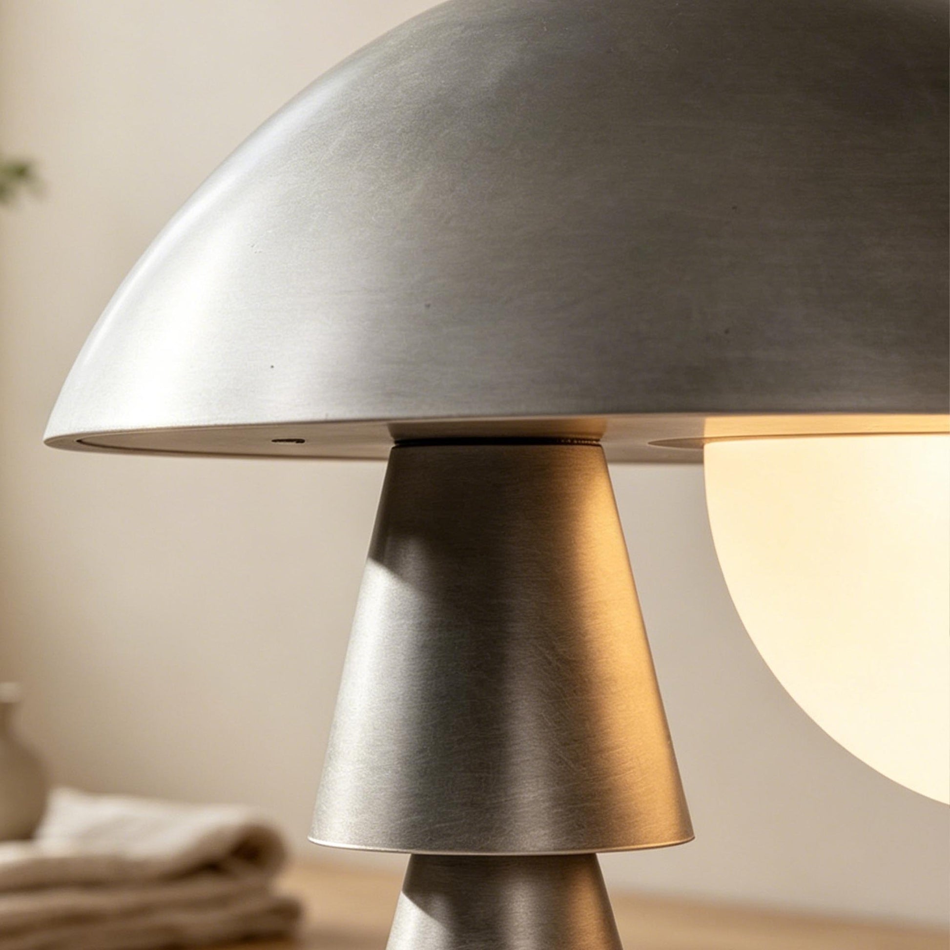 Close-up of the silver metal dome shade and glowing frosted glass diffuser on the sculptural table lamp